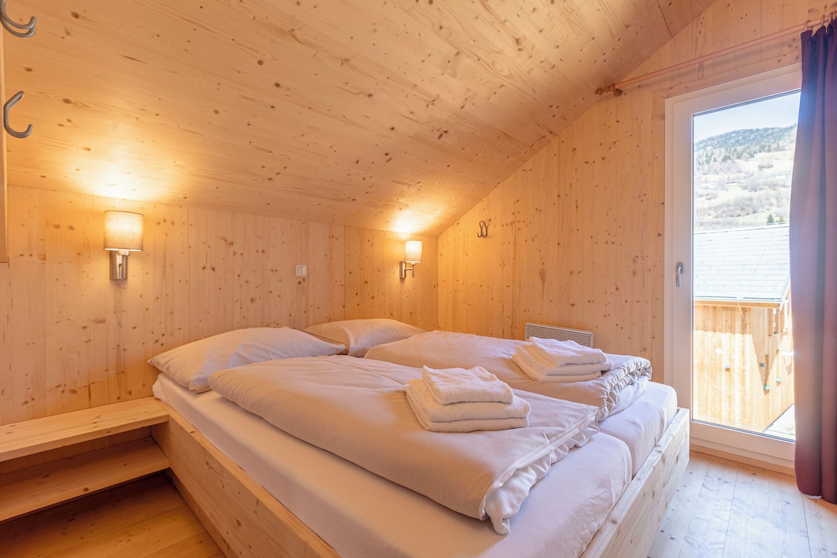 A wooden cabin bedroom with two beds, each with white linens and towels, and two wall-mounted lamps.
