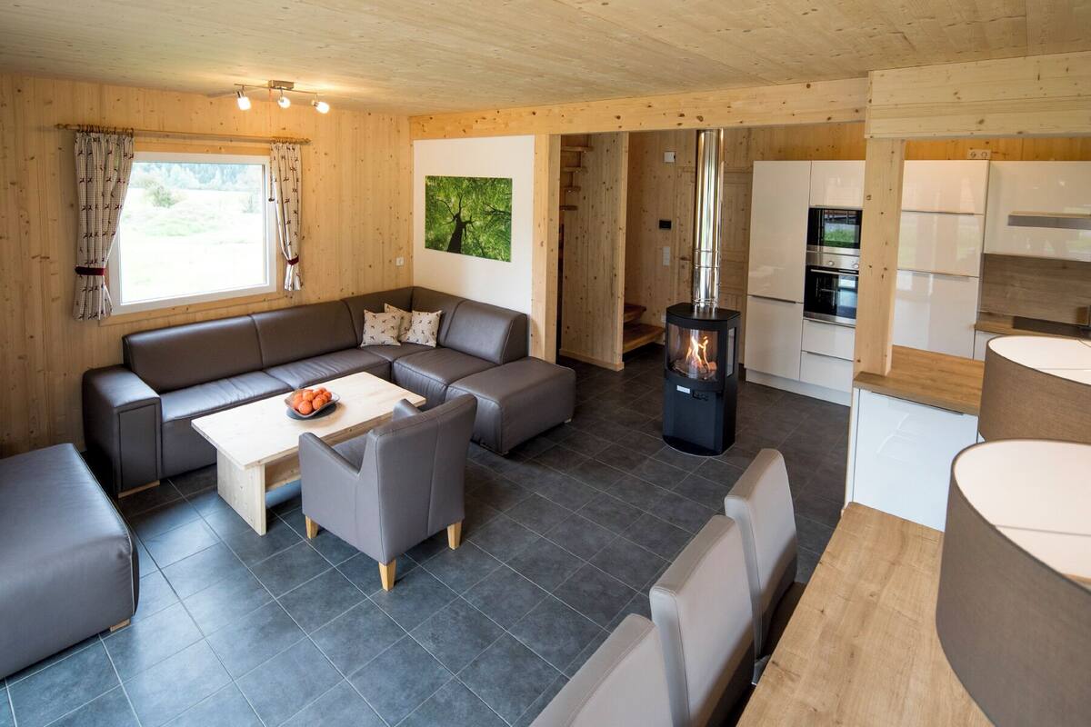 Interior moderno de cabaña con detalles de madera, un conjunto de sofás, una mesa de comedor, una zona de cocina y una chimenea.