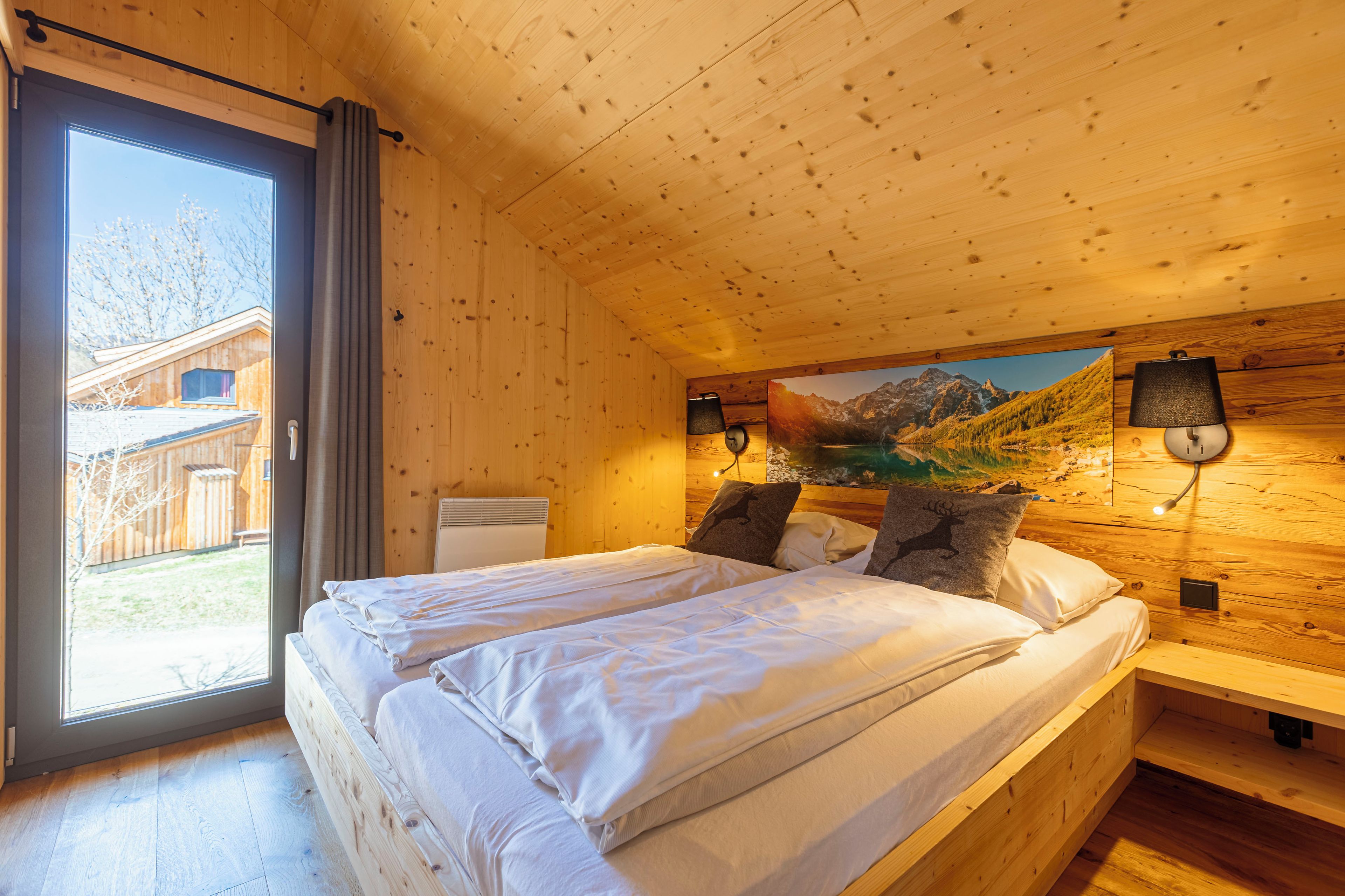 Ein Holzinnenraum mit einem Bett, einem Fenster und einer Wandleuchte.