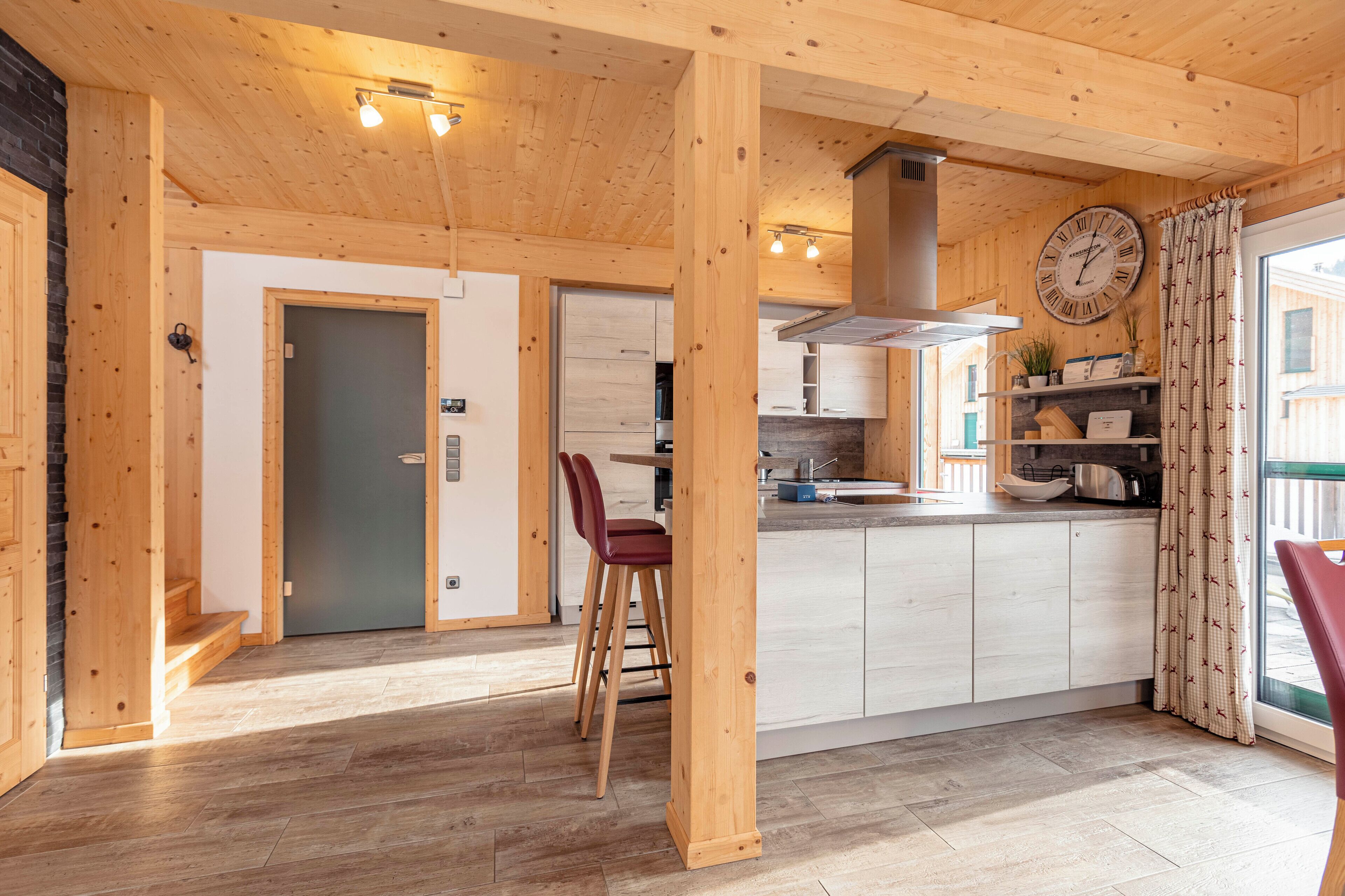 A wooden interior with a kitchen, dining area, and a large clock on the wall.