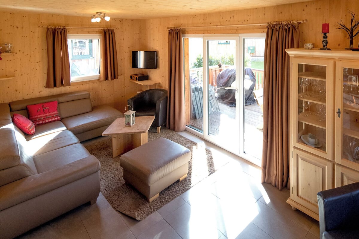 A cozy living room with a sofa, ottoman, and a flat-screen TV mounted on the wall.