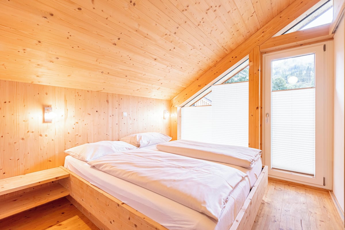 Dormitorio de cabaña de madera con cama, banco empotrado y tragaluz.