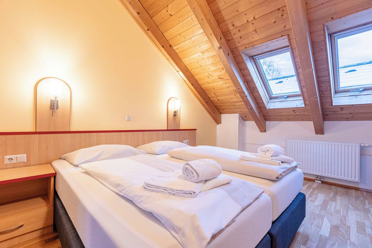 Ein Hotelzimmer mit zwei Betten, Holzbalkendecke, Dachfenstern und einer Heizung.