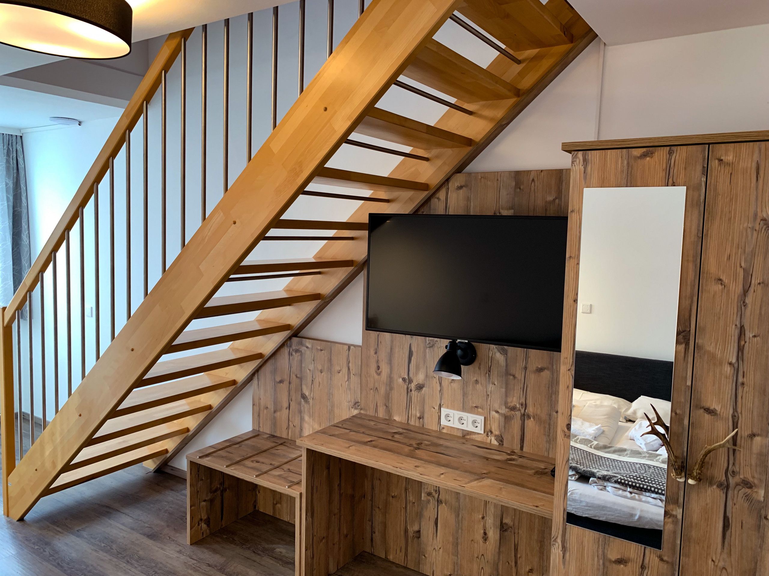 A modern interior with a wooden staircase, a mounted flat-screen TV, and a built-in wooden cabinet with a mirror.