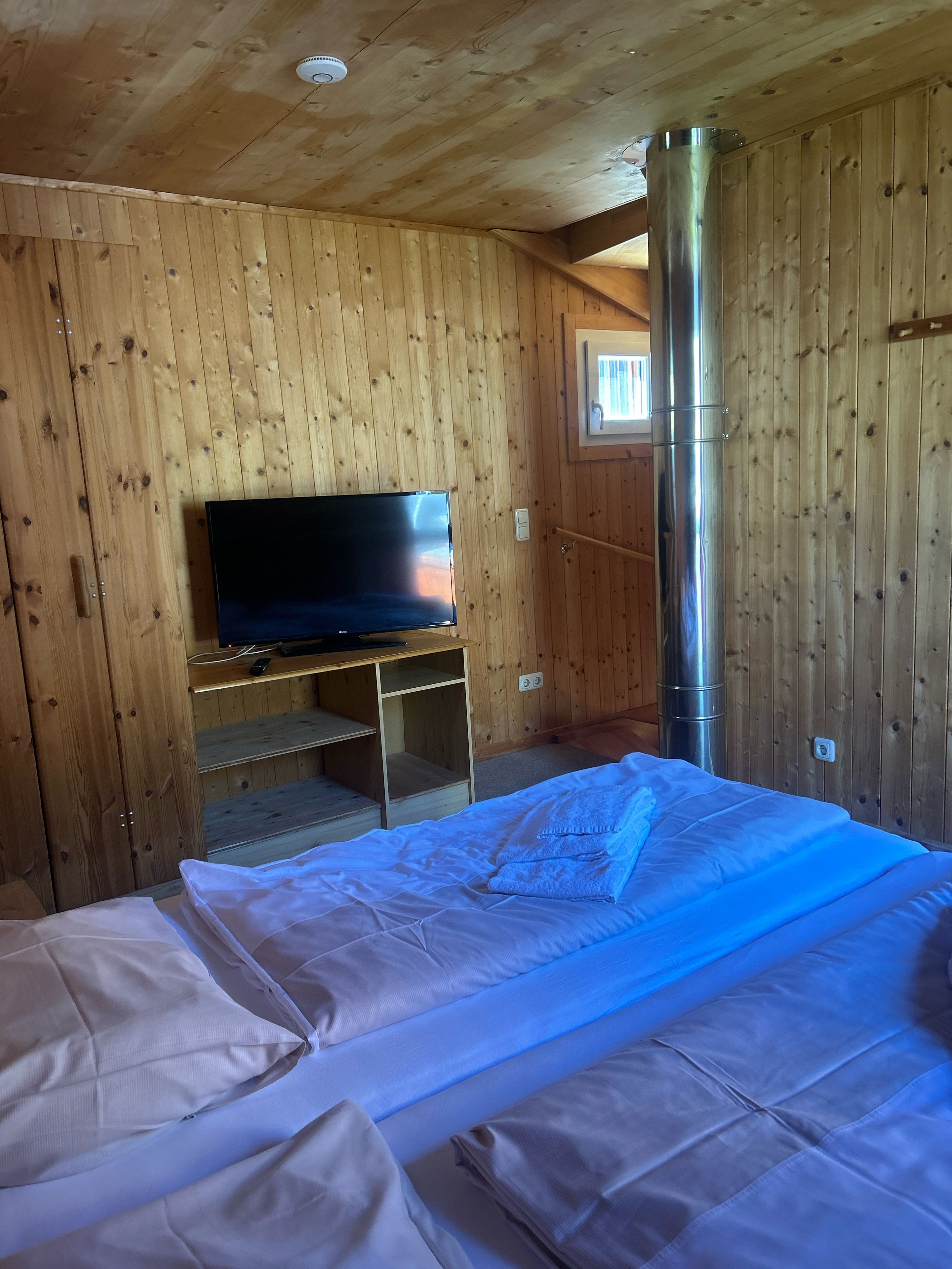 A wooden-paneled room with a bed, a television on a stand, and a large cylindrical object, possibly a heater.