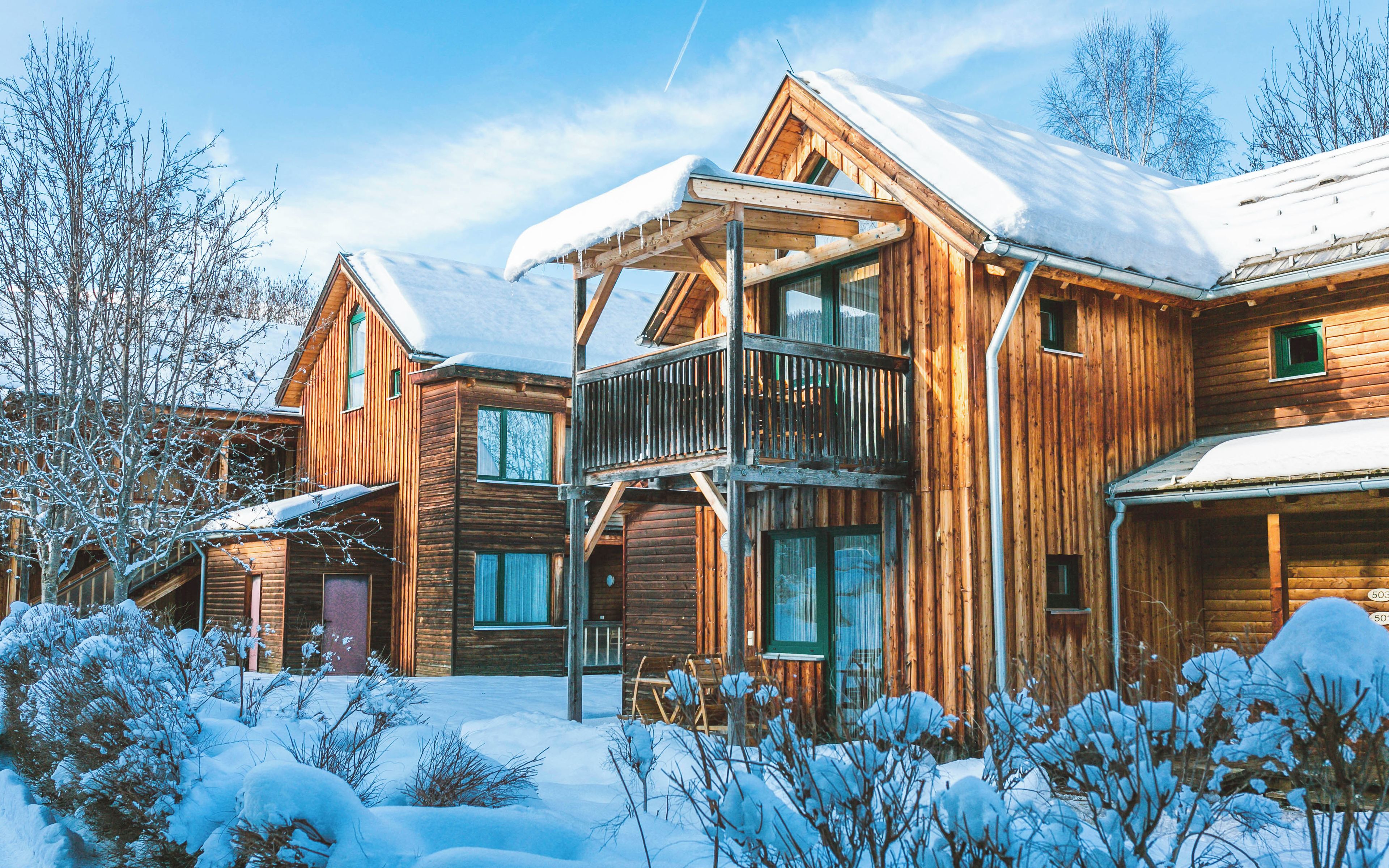 A wooden cabin with a balcony, multiple windows, and a snow-covered landscape.