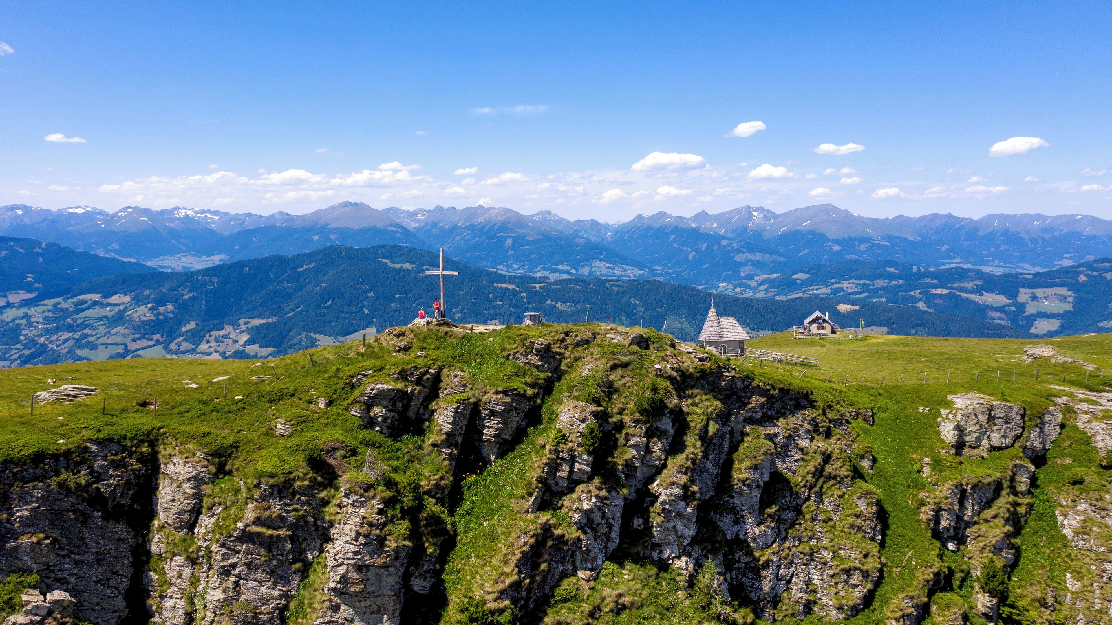 A mountain landscape with a chapel and a cross on a hilltop.