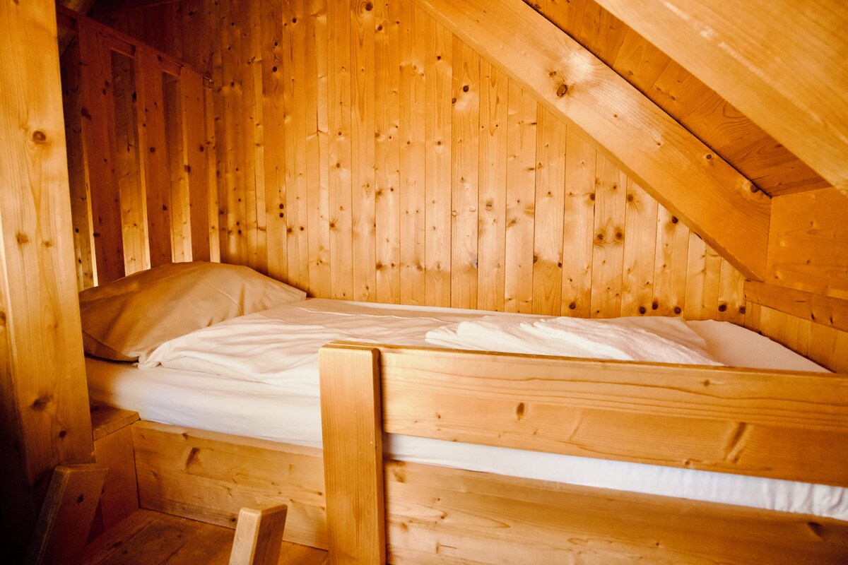 Ein Holzbett mit Etagen in einer Holzhütte mit geneigter Decke und Holzwänden.