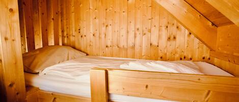 Una cama litera de madera en una cabaña con techo inclinado y paredes de madera.