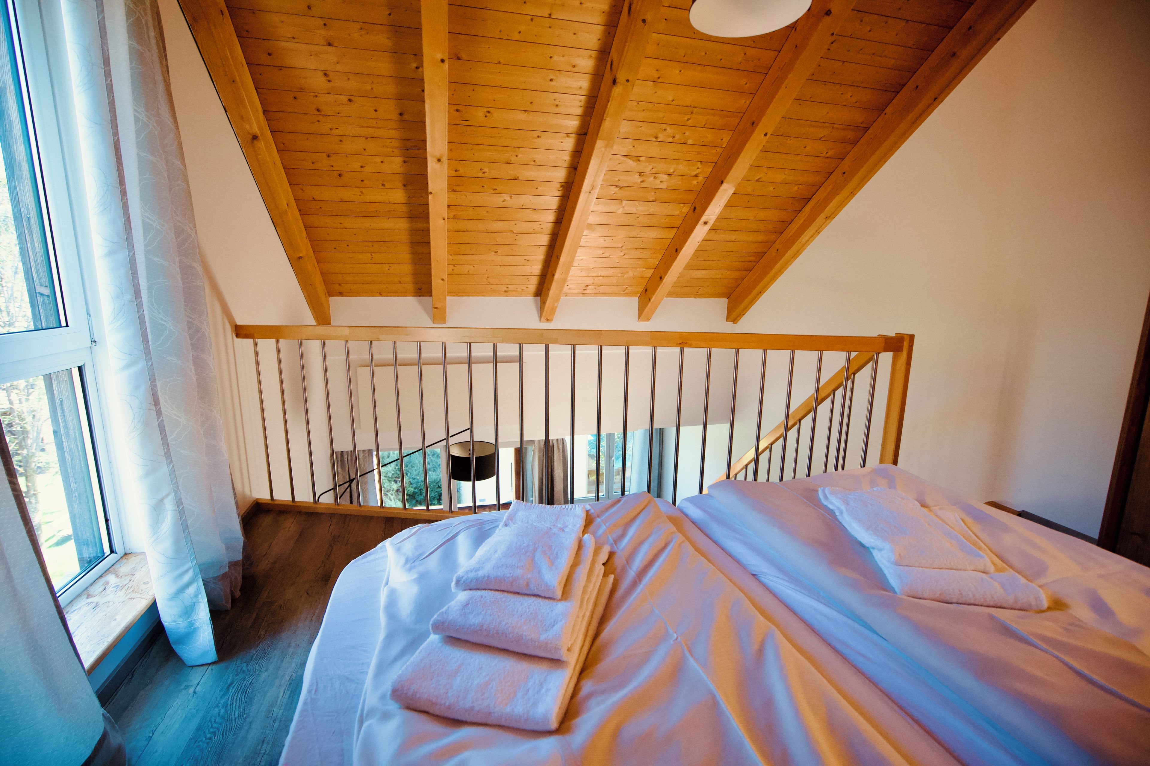 A bedroom with a wooden ceiling, a bed with white bedding, and a window with curtains.