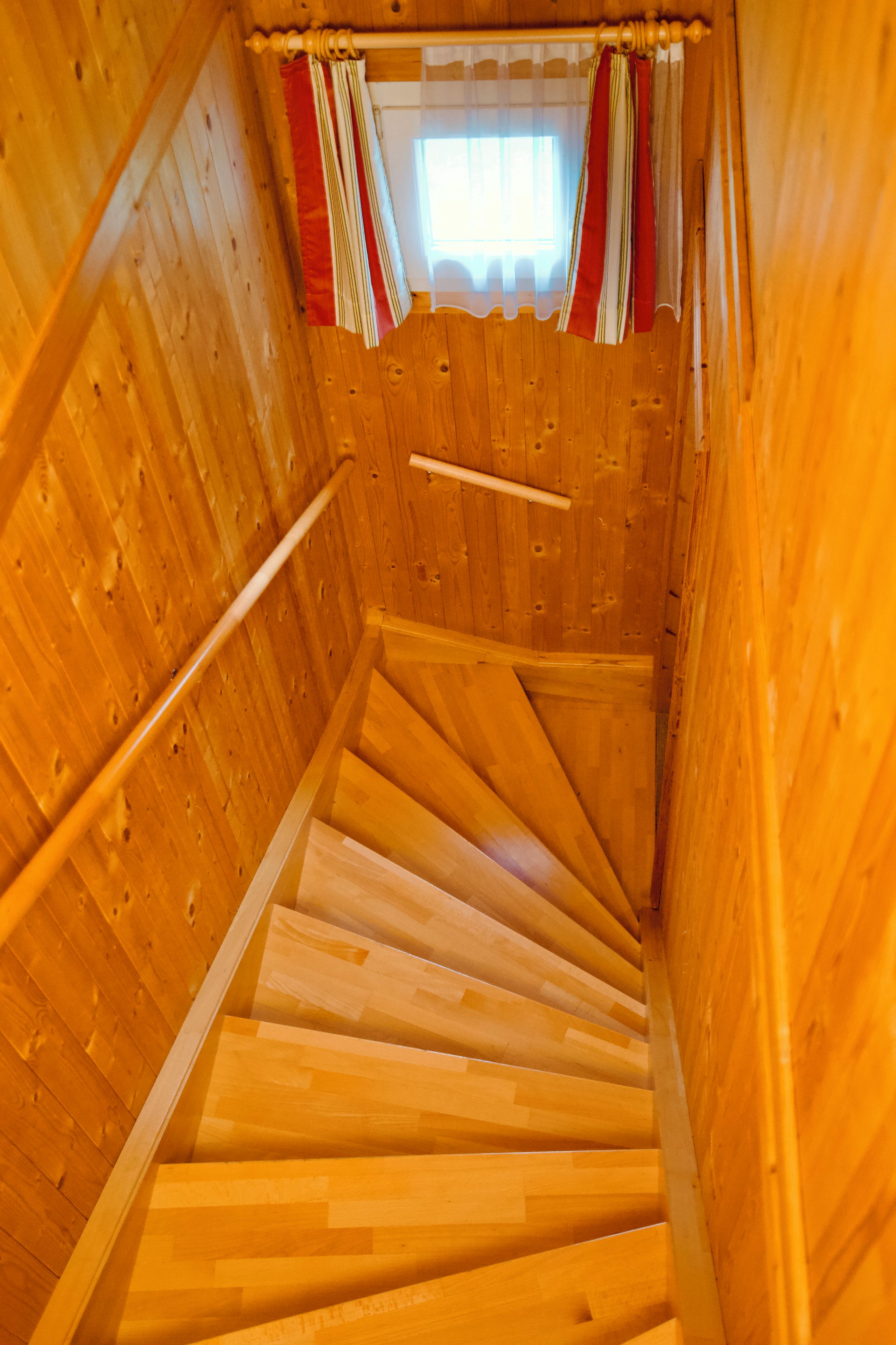 A wooden interior with a spiral staircase leading to a window with curtains.