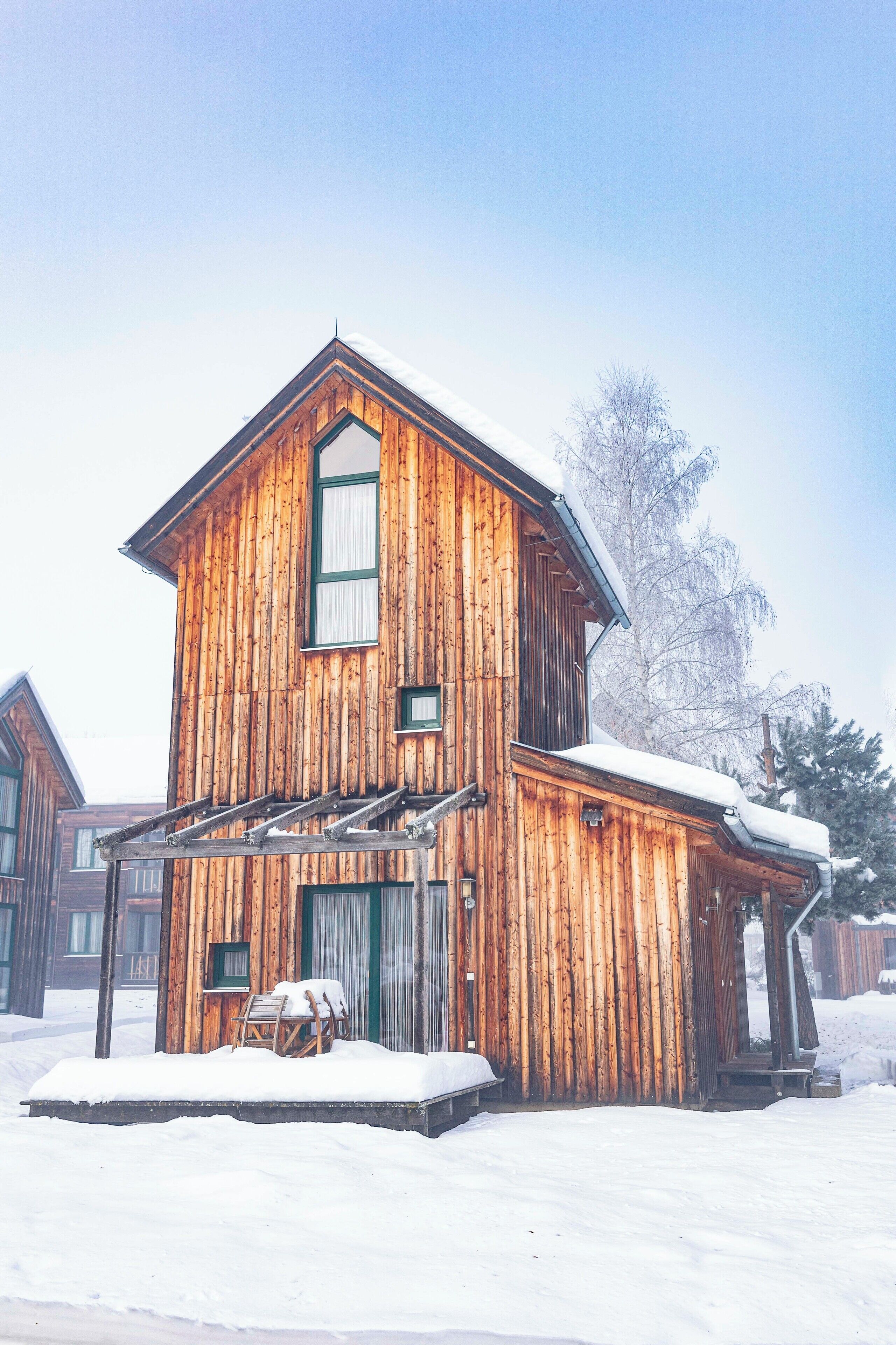 Een houten hut met veranda en een overdekt terras, omgeven door sneeuw.