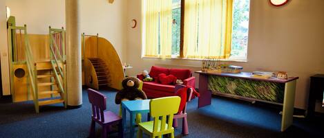A children's playroom with a wooden staircase, colorful chairs, a table, and a window with curtains.