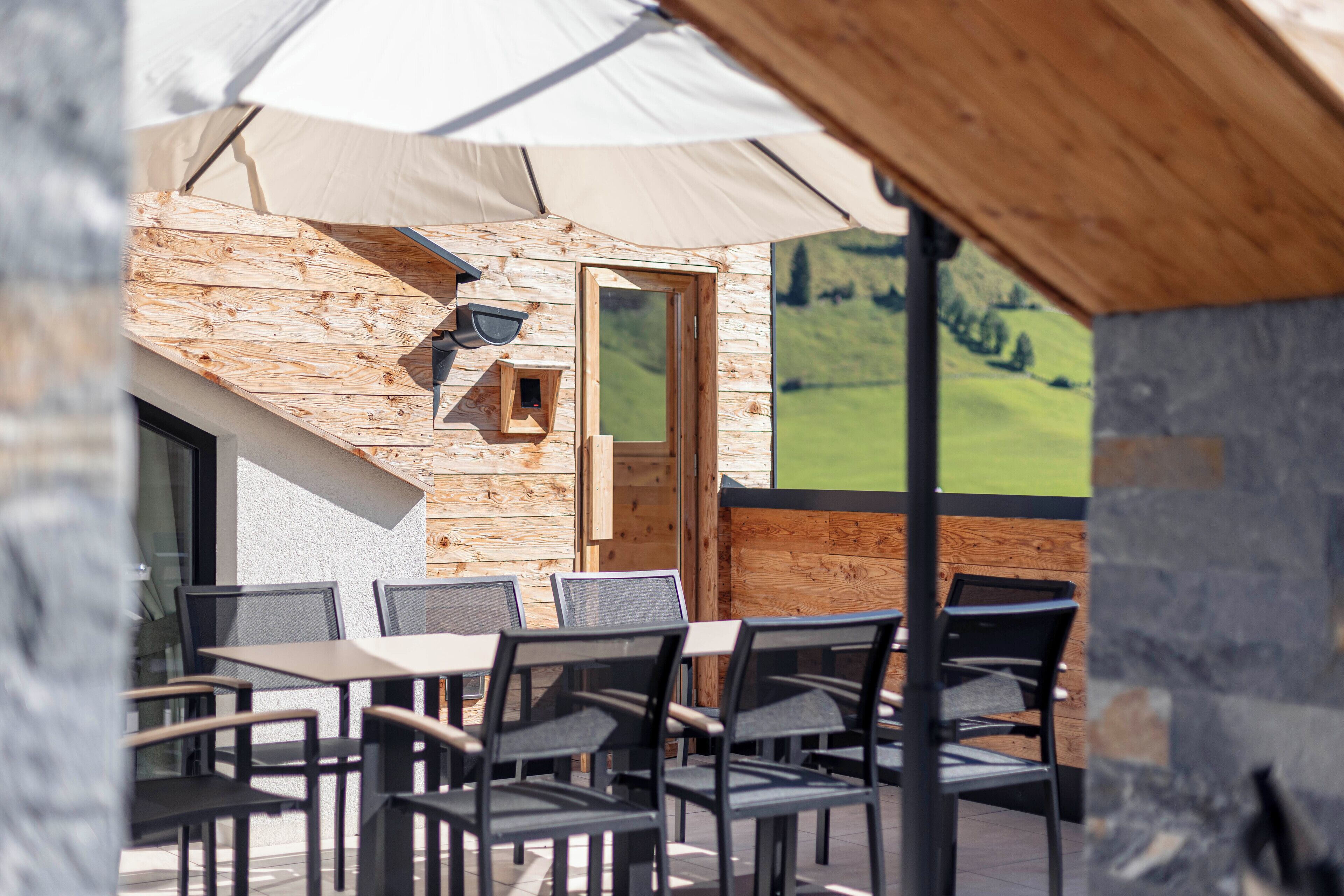 Un área de estar al aire libre con mesas y sillas de madera, un muro de madera y una puerta.