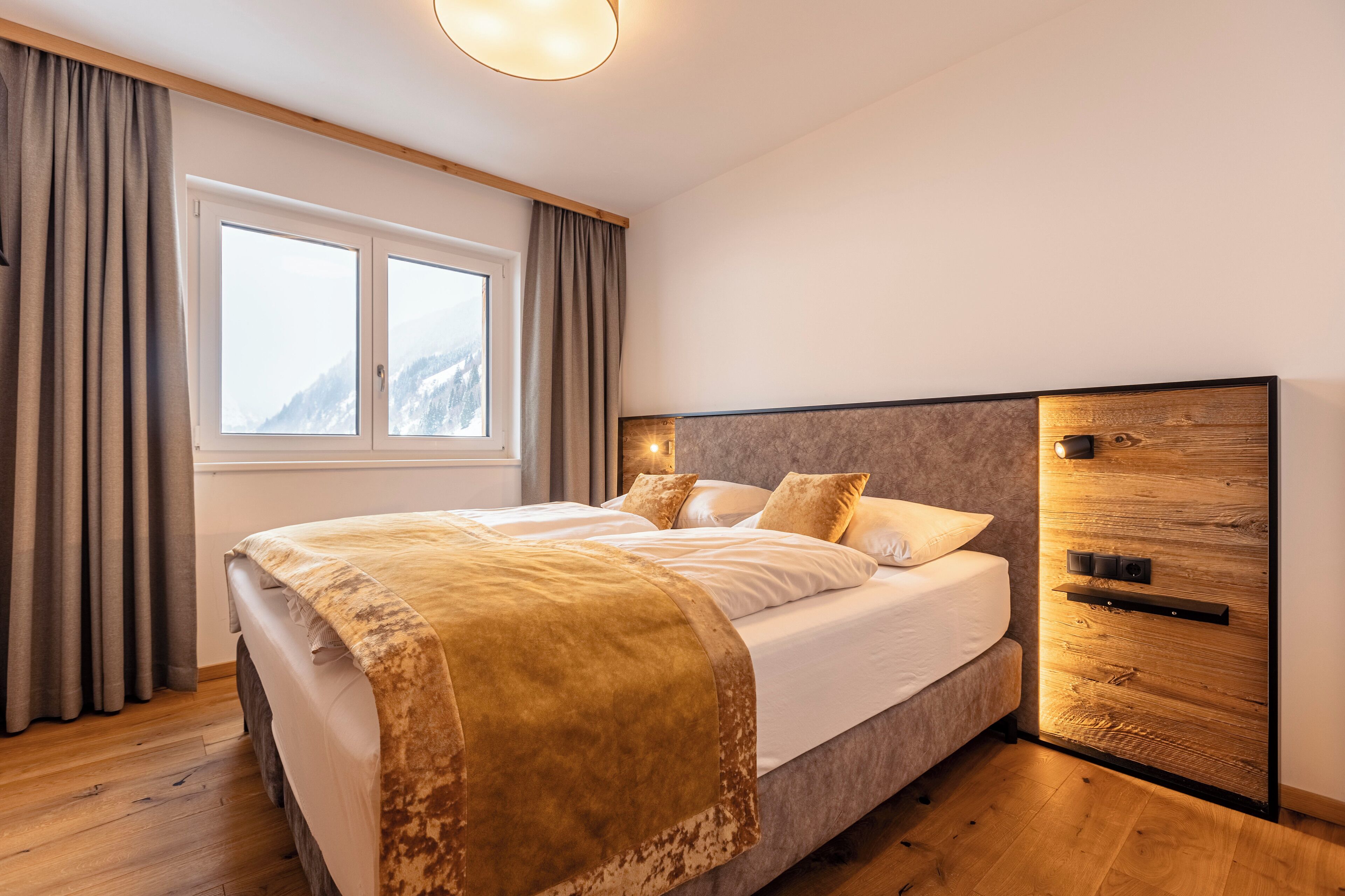 Une chambre avec un grand lit, une armoire en bois, une fenêtre avec des rideaux et une vue sur la montagne.