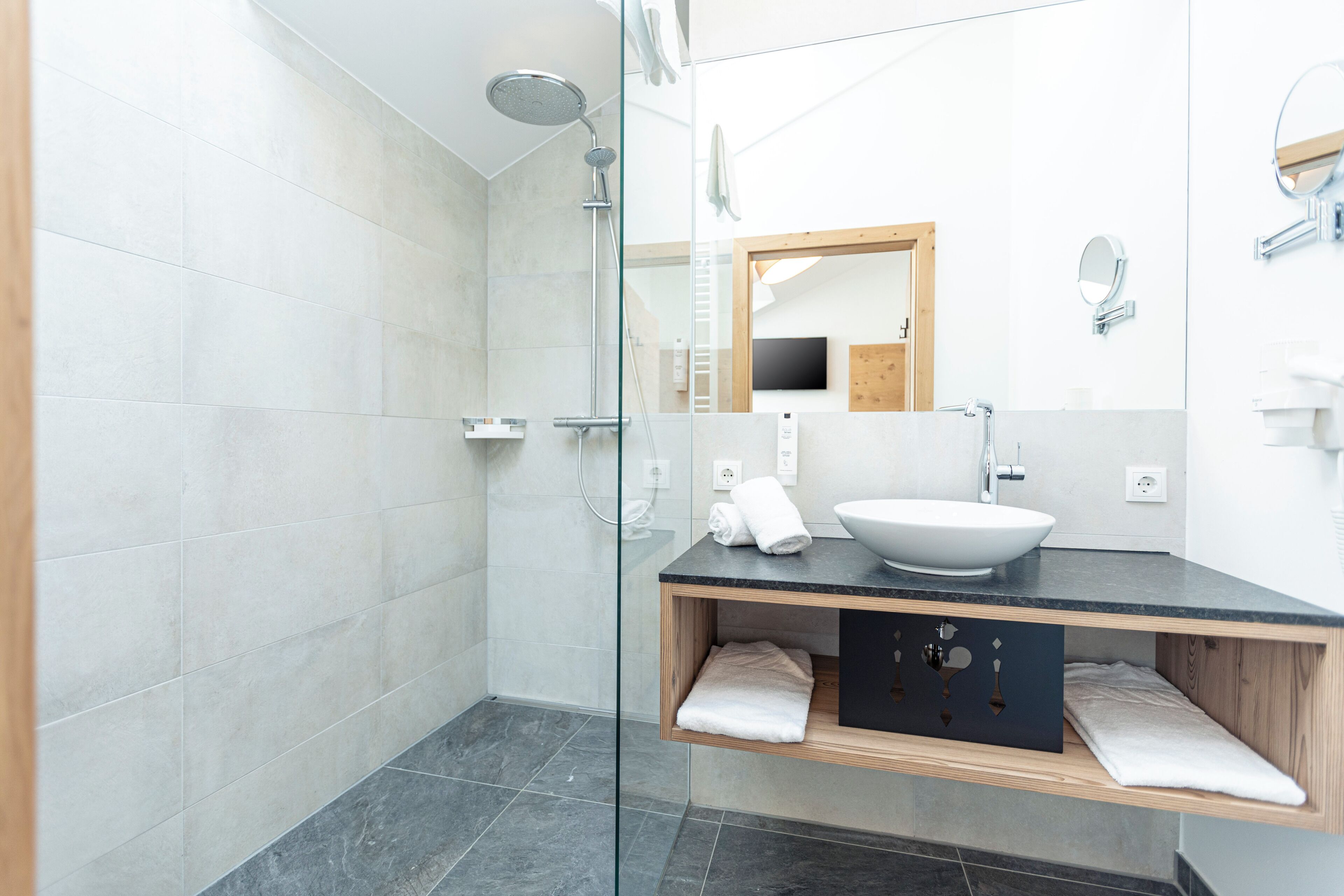 Un bany modern amb una dutxa amb envàs de vidre, un lavabo blanc i un moble de tocador de fusta.