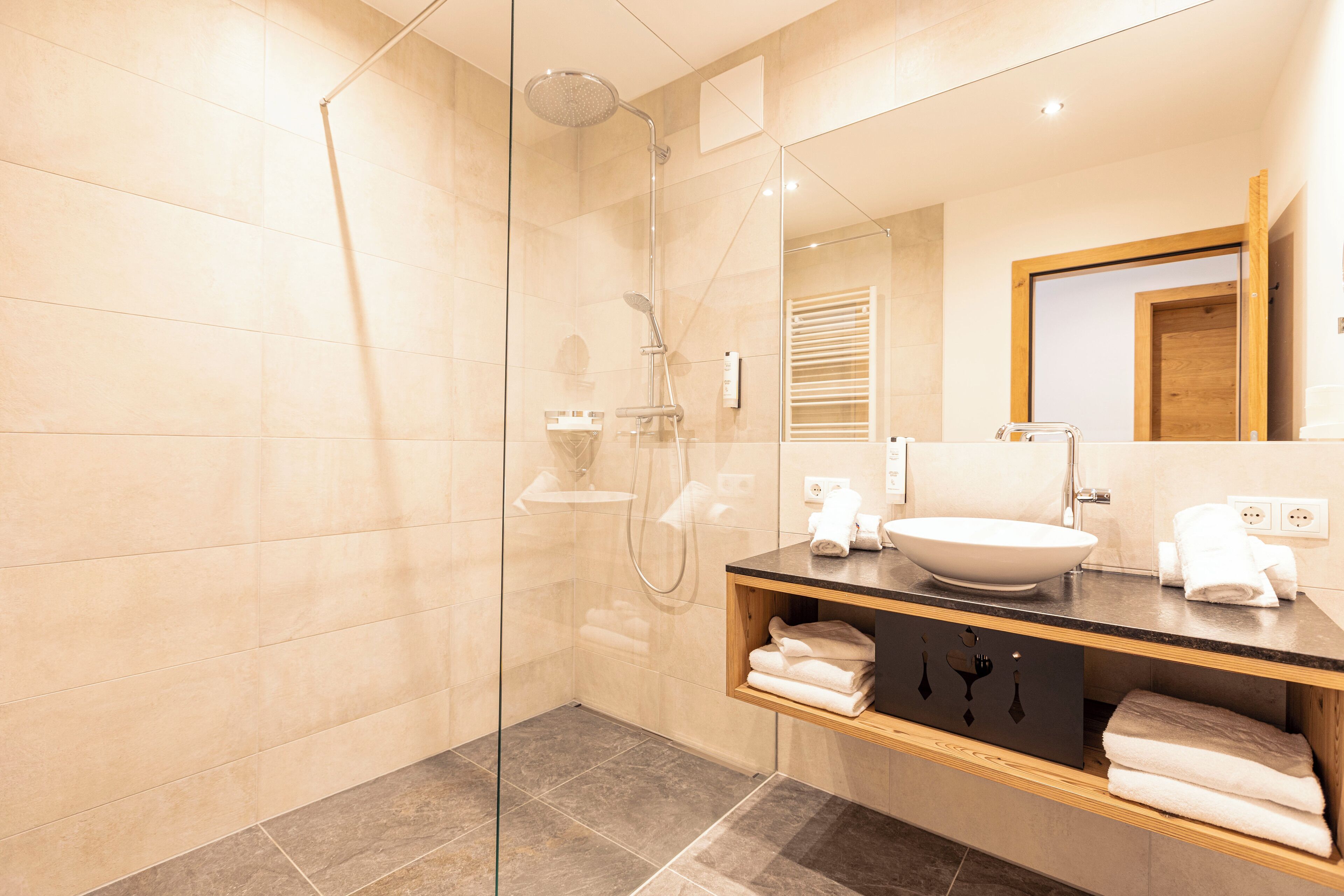 A modern bathroom with a glass-enclosed shower, a sink with a vessel basin, and a wooden vanity with towels.