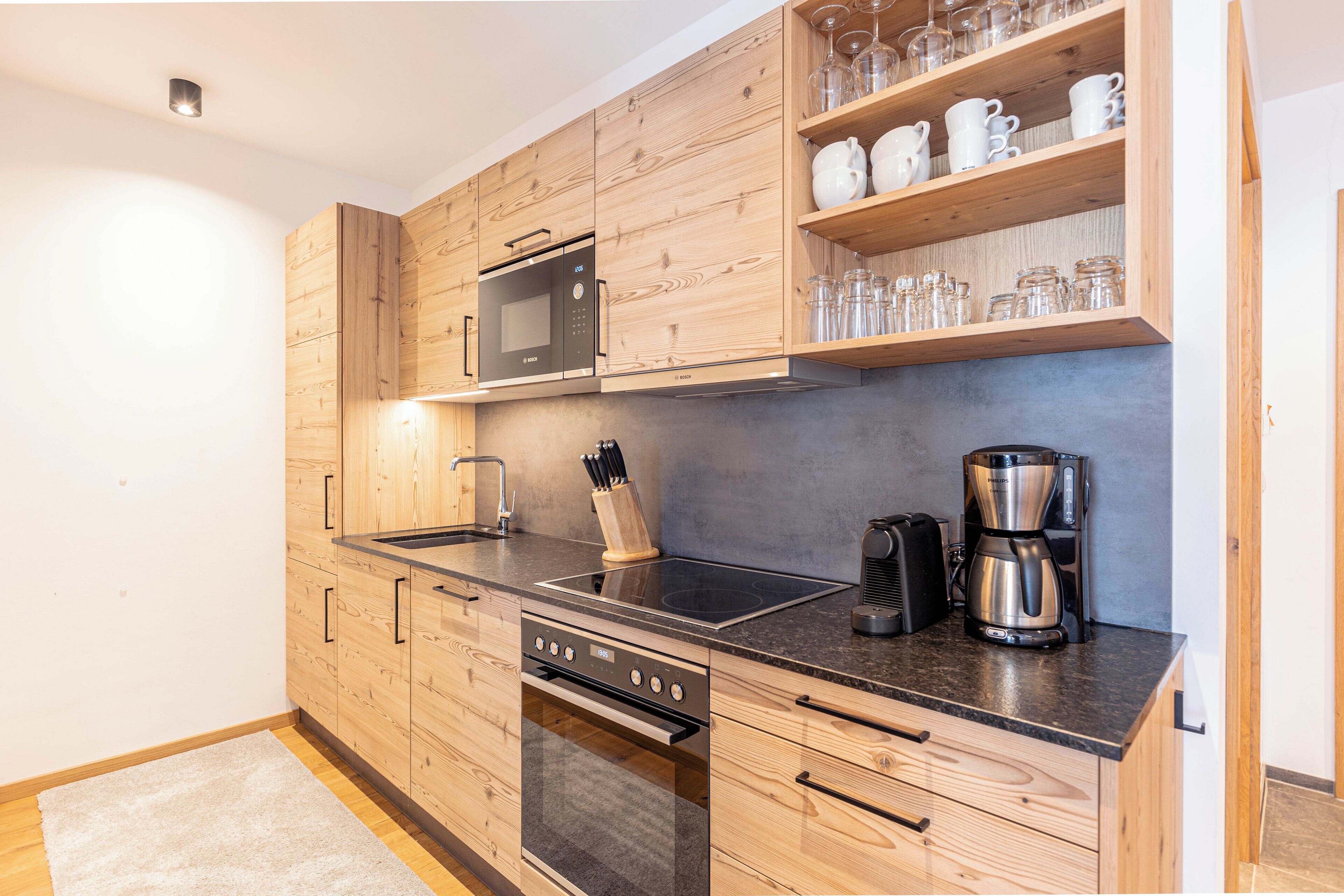 A modern kitchen with wooden cabinets, a built-in microwave, a coffee maker, and a knife block.