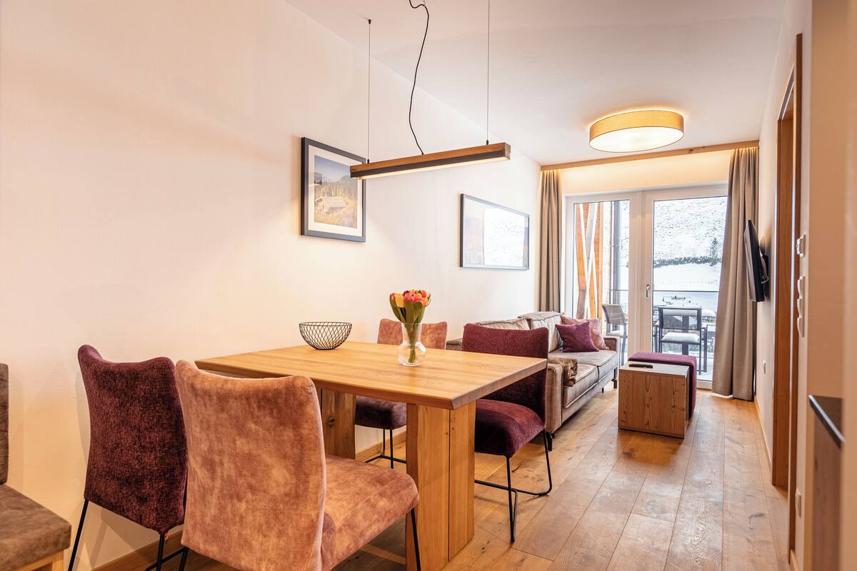A modern dining area with a wooden table, cushioned chairs, and a vase of flowers.