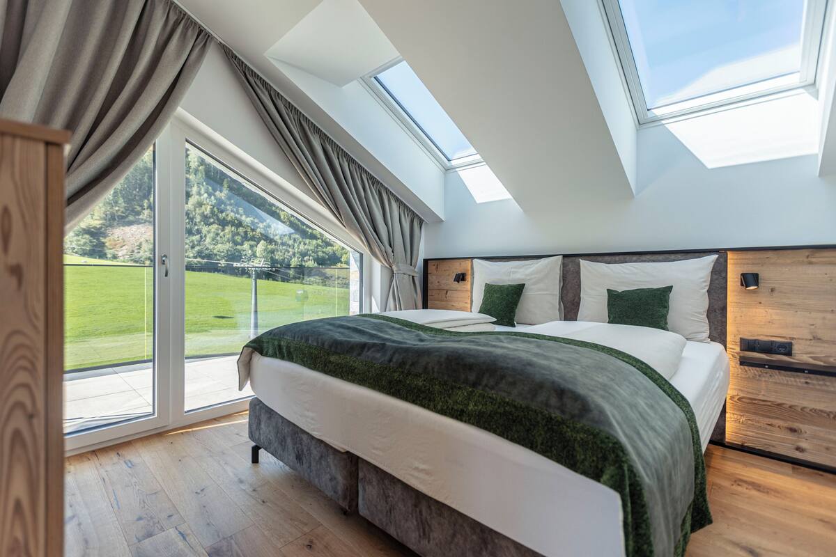 A bedroom with a large bed, skylight windows, and a view of a green landscape.