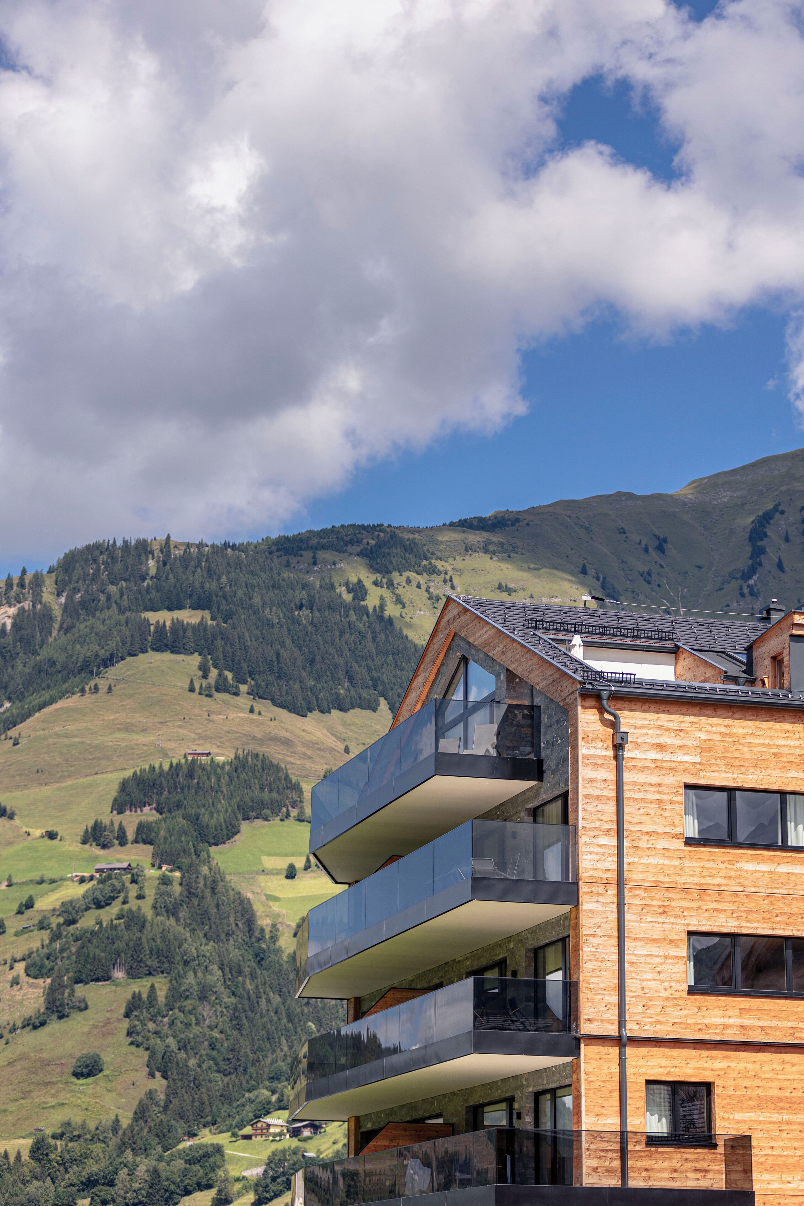 A modern building with multiple balconies, set against a backdrop of a mountainous landscape.