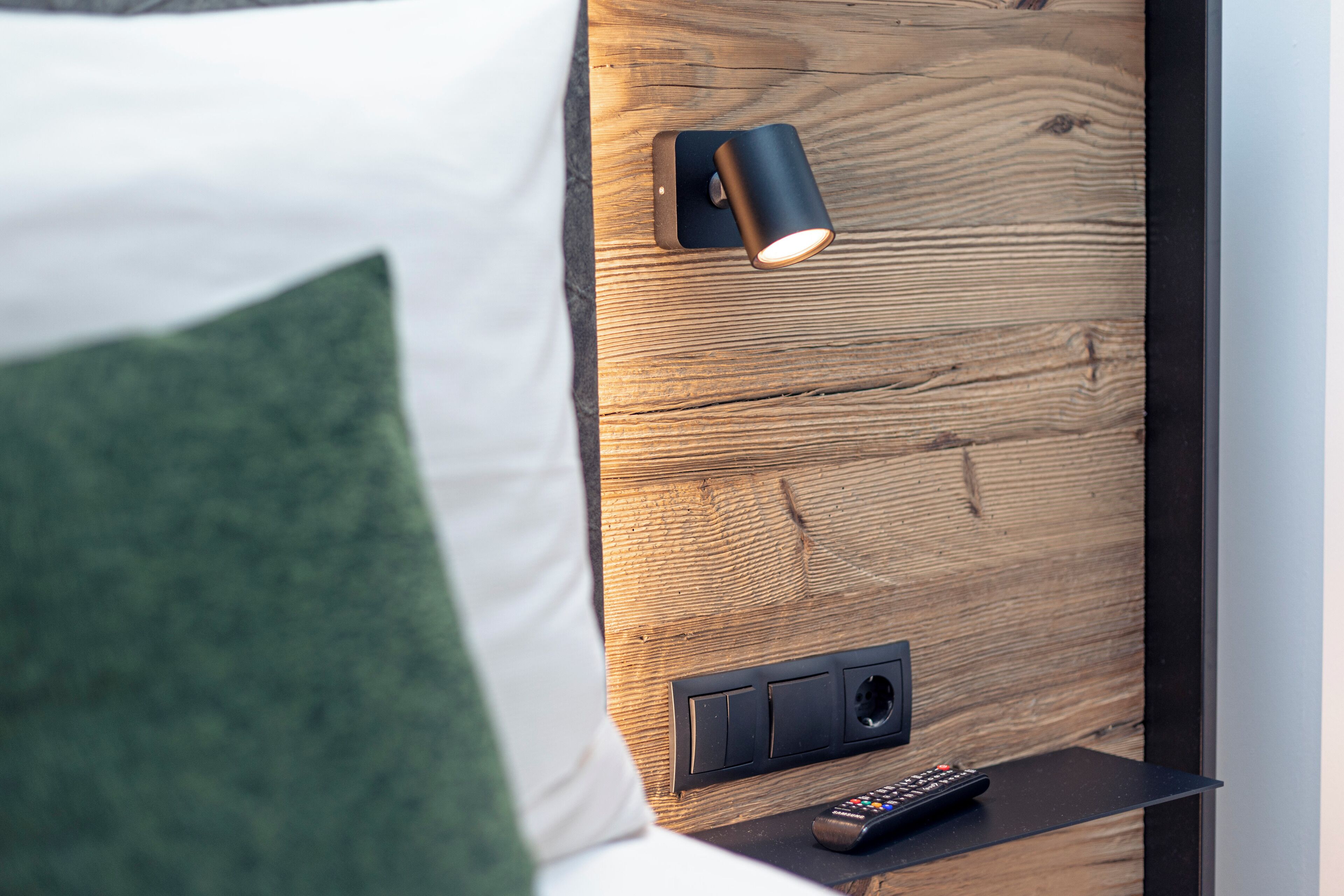 A wooden headboard with a wall-mounted light fixture and a remote control on a bedside table.