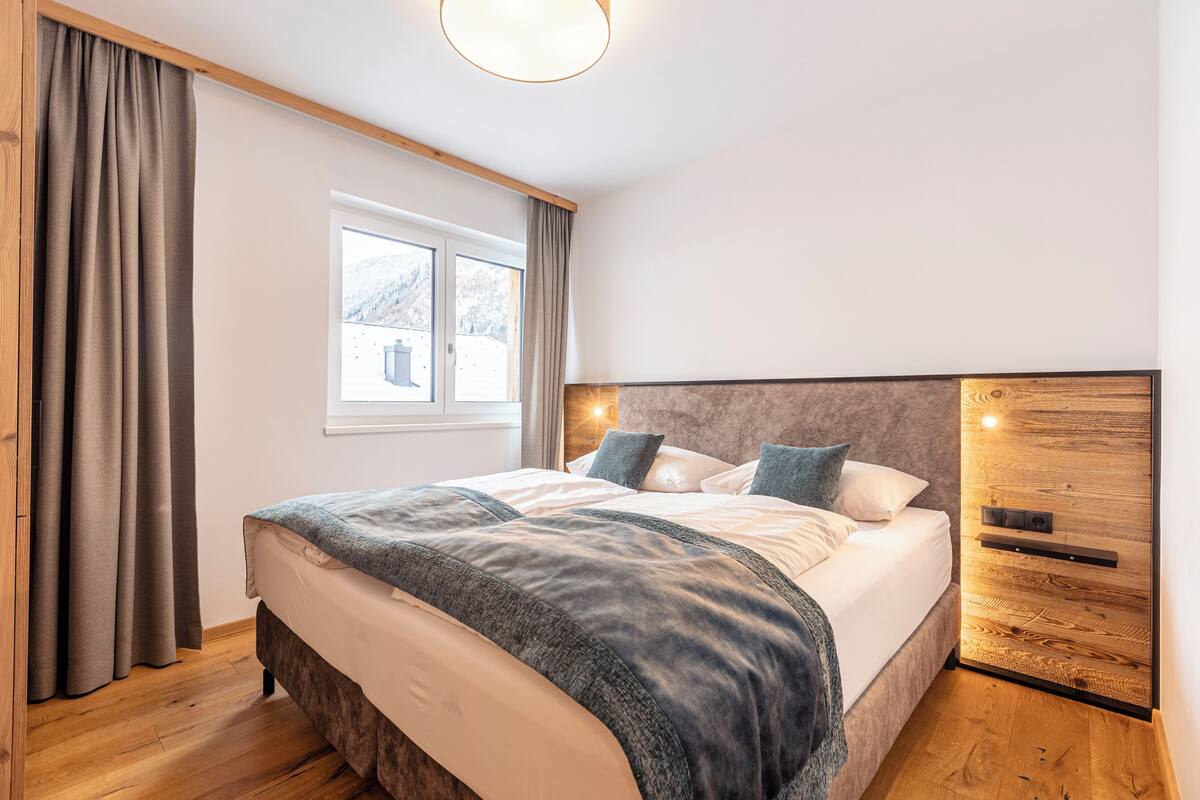 A modern bedroom with a large bed, wooden headboard, and a window with curtains.