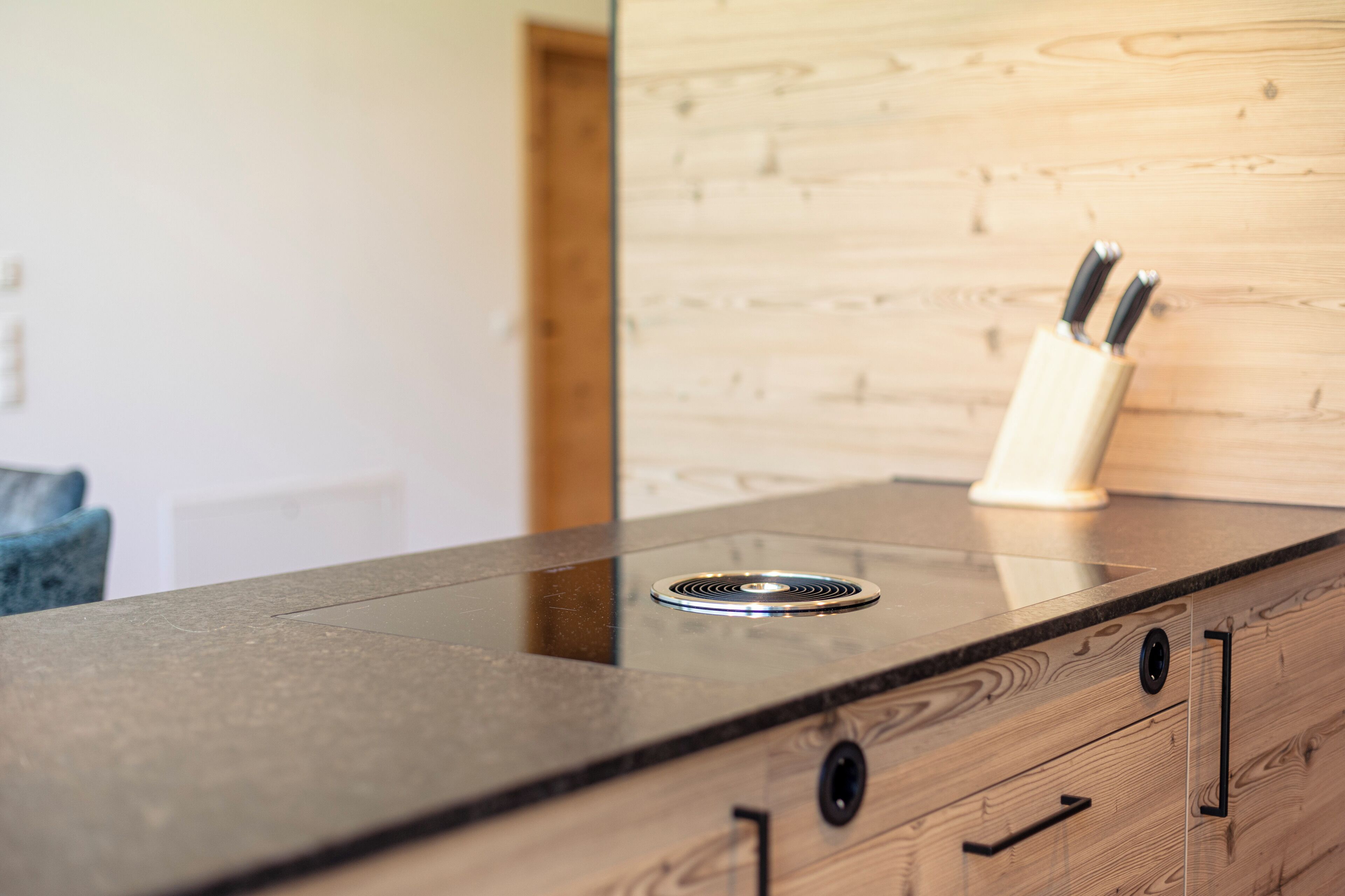 A kitchen counter with a built-in stove, wooden cabinetry, and a knife block.