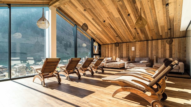 A sunlit room with wooden flooring, a wooden ceiling, and large windows overlooking a cityscape. - Carpe Solem Rauris by ALPS RESORTS (Rauris)