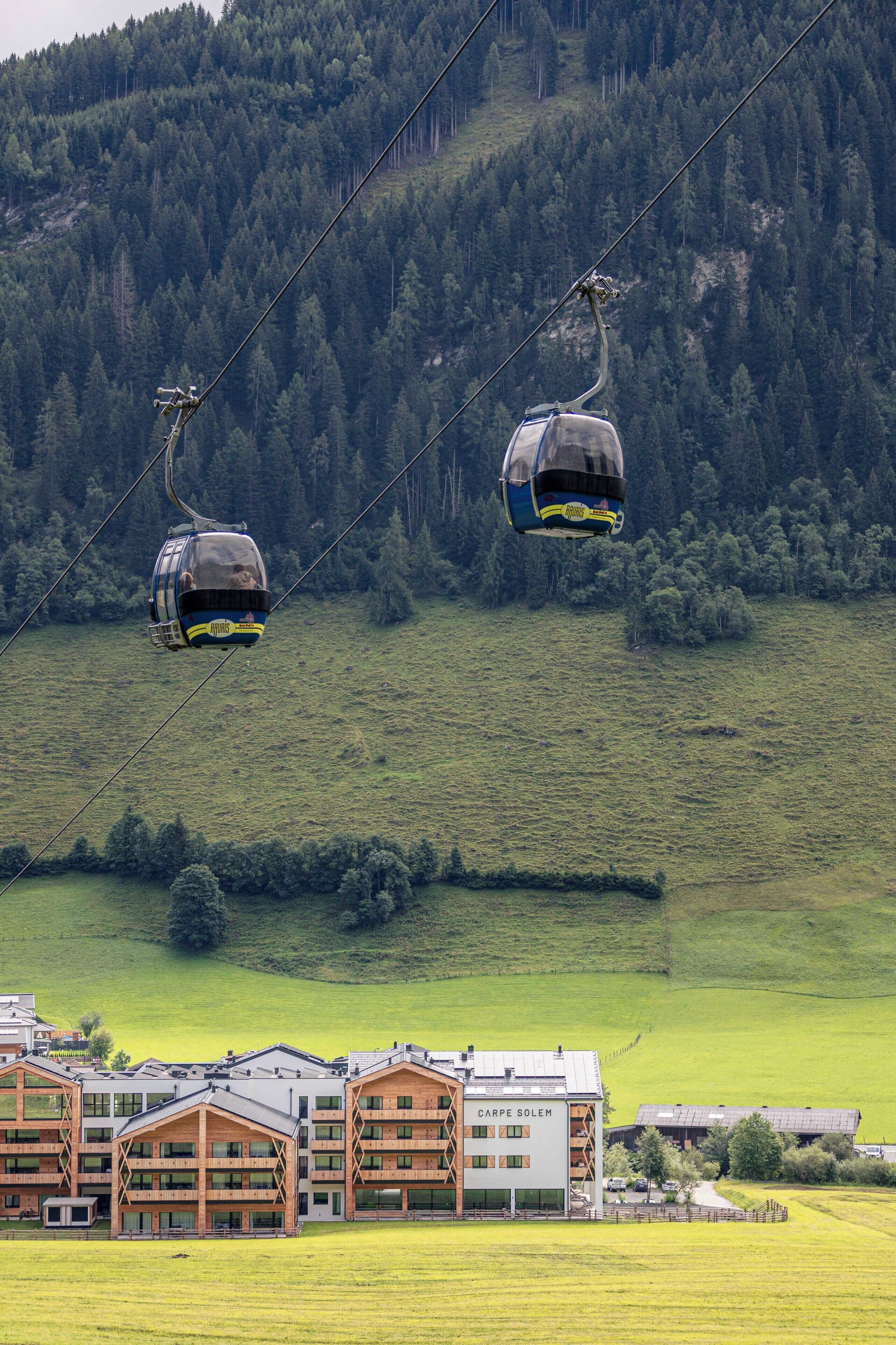 A cable car system in a mountainous area with a building labeled "CARPE SOLEM" in the foreground.
