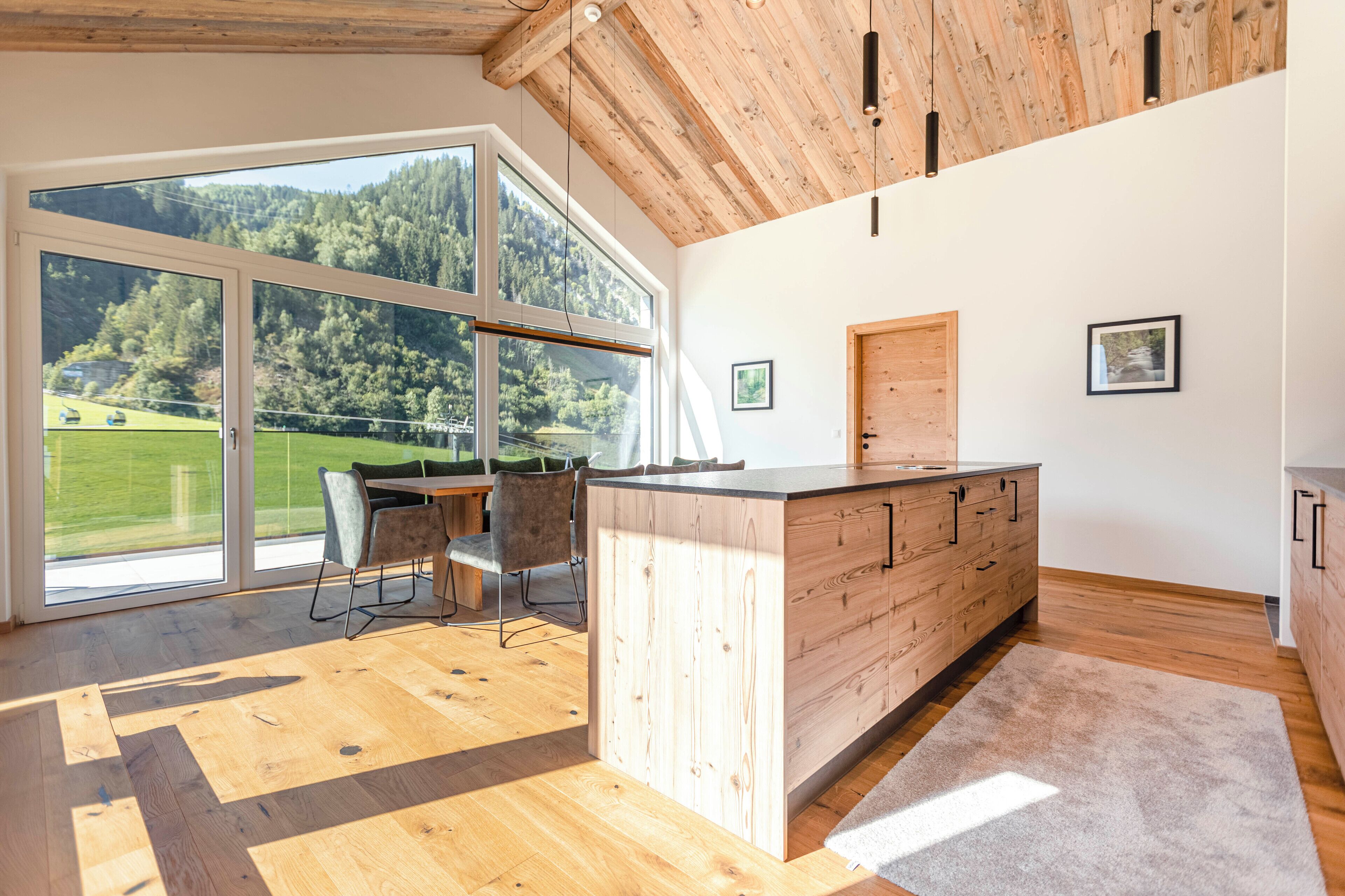 Een moderne keuken met grote ramen, houten vloeren en uitzicht op een groen landschap.