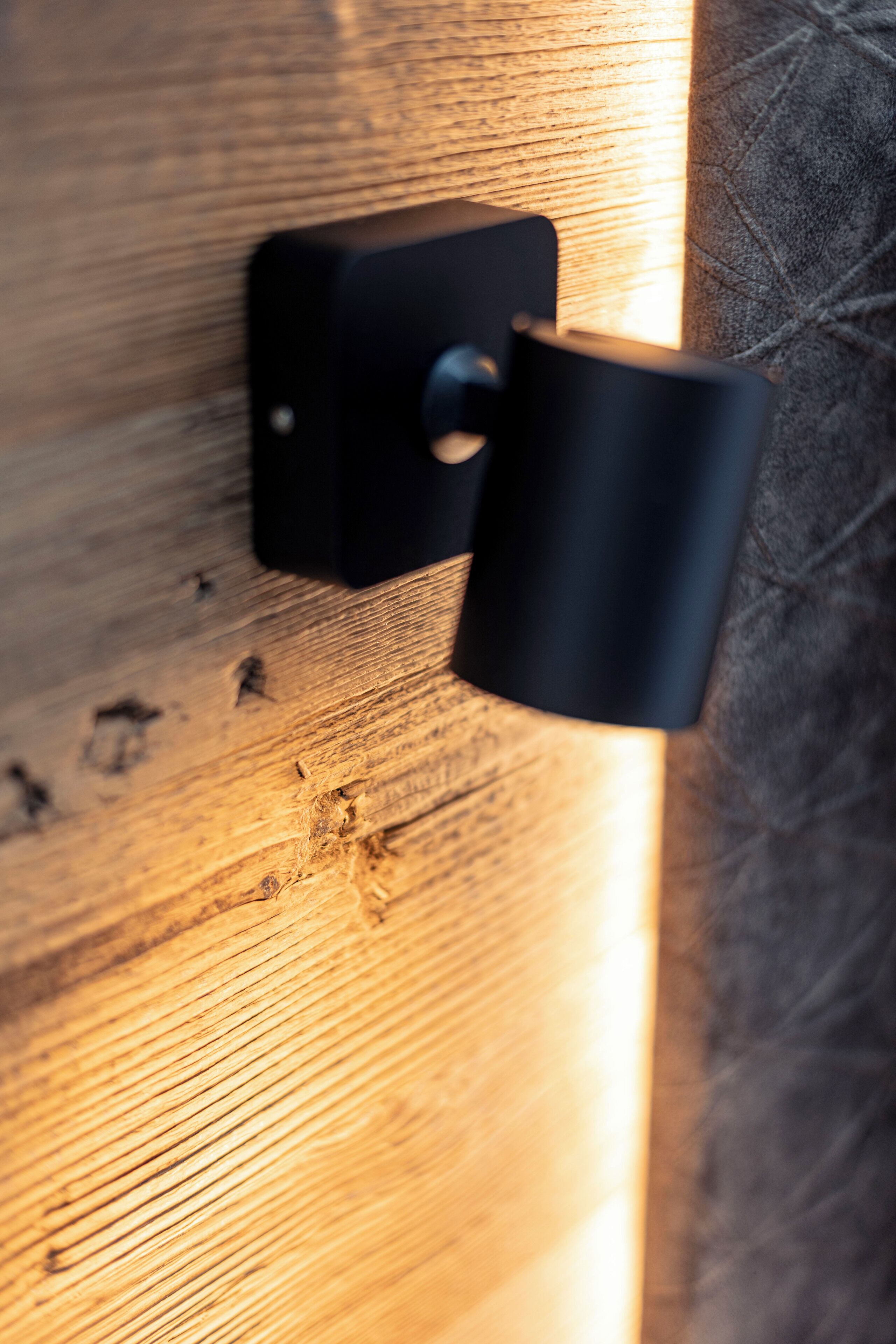 A close-up of a black wall-mounted light fixture on a wooden surface.