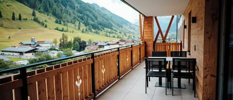 Un balcone con ringhiera in legno, un tavolo con sedie e vista su un paesaggio montuoso.