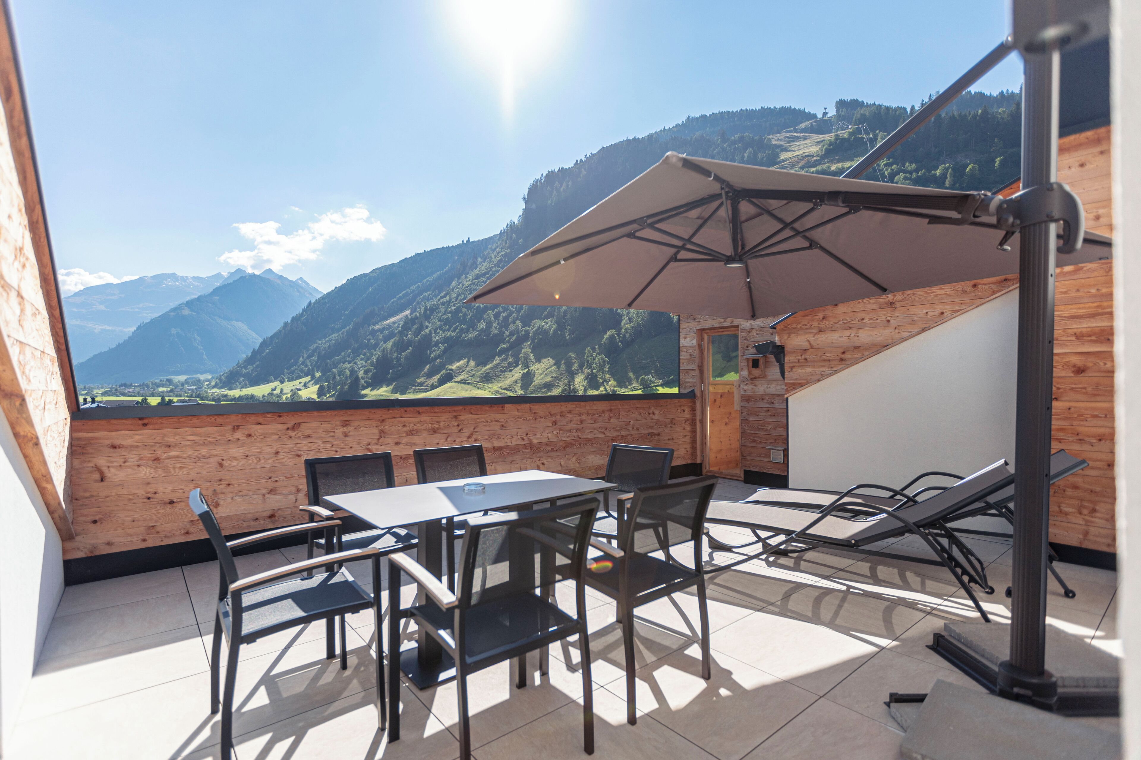 A terrace with a table and chairs, a sun umbrella, and a view of mountains.