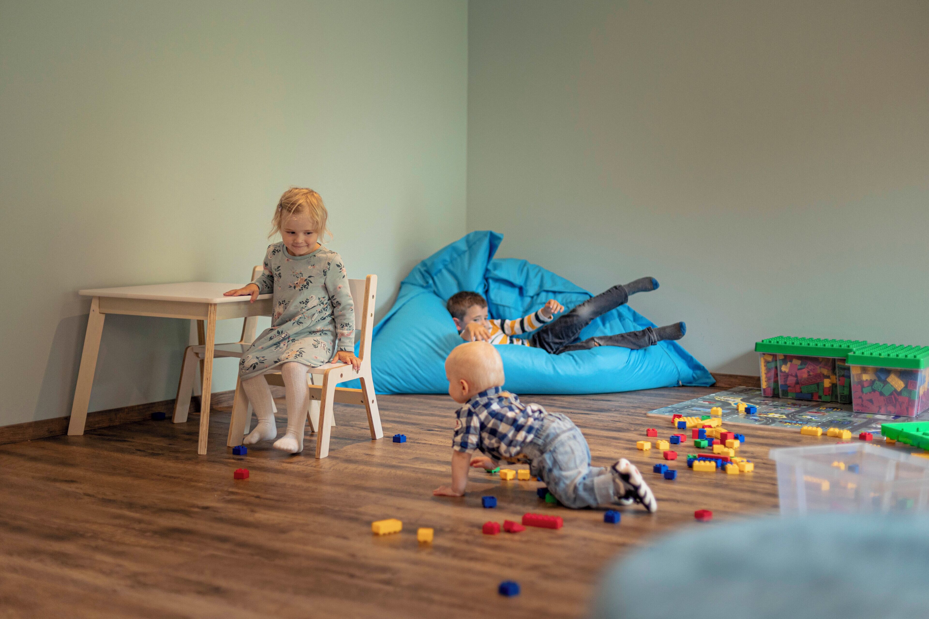 Una habitación con piso de madera, un sillón colgante azul y una mesa con un niño sentado.