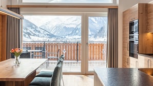 A modern kitchen with wooden cabinets and a large window overlooking a snowy mountain landscape. - Carpe Solem Rauris by ALPS RESORTS (Rauris)