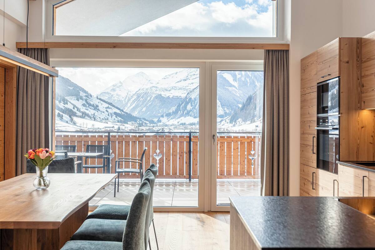 A modern kitchen with wooden cabinets and a large window overlooking a snowy mountain landscape.
