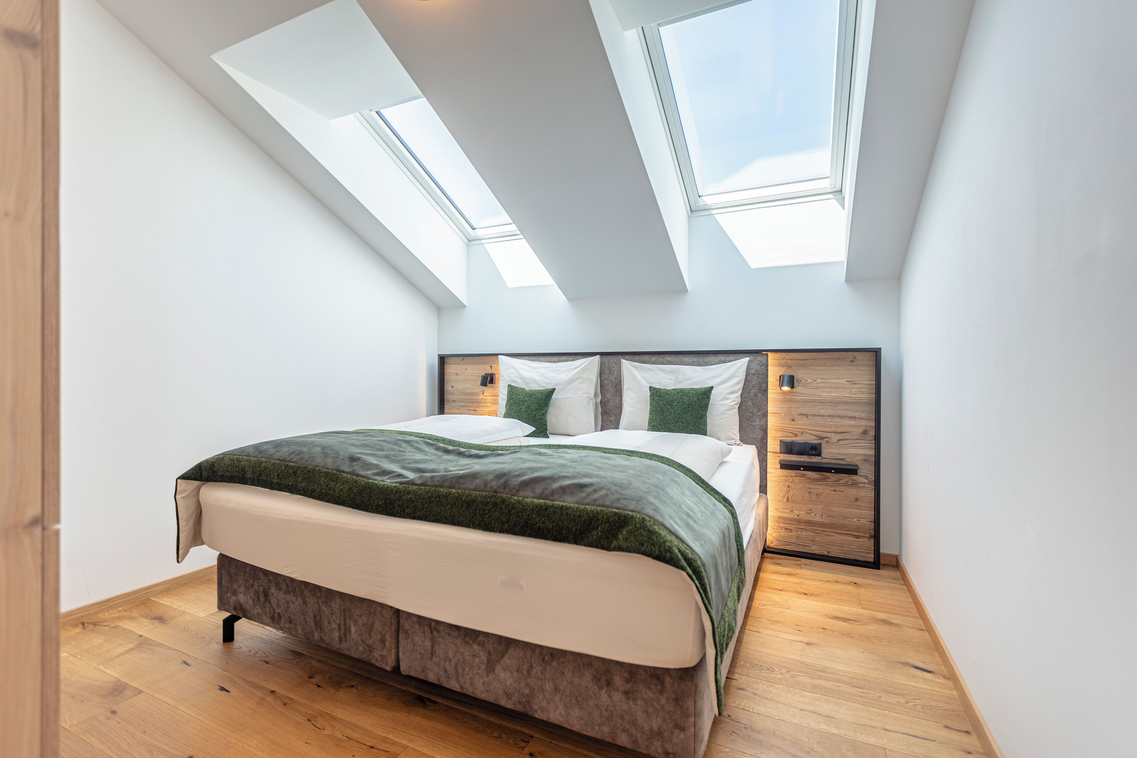 A bedroom with a bed, skylights, and wooden flooring.