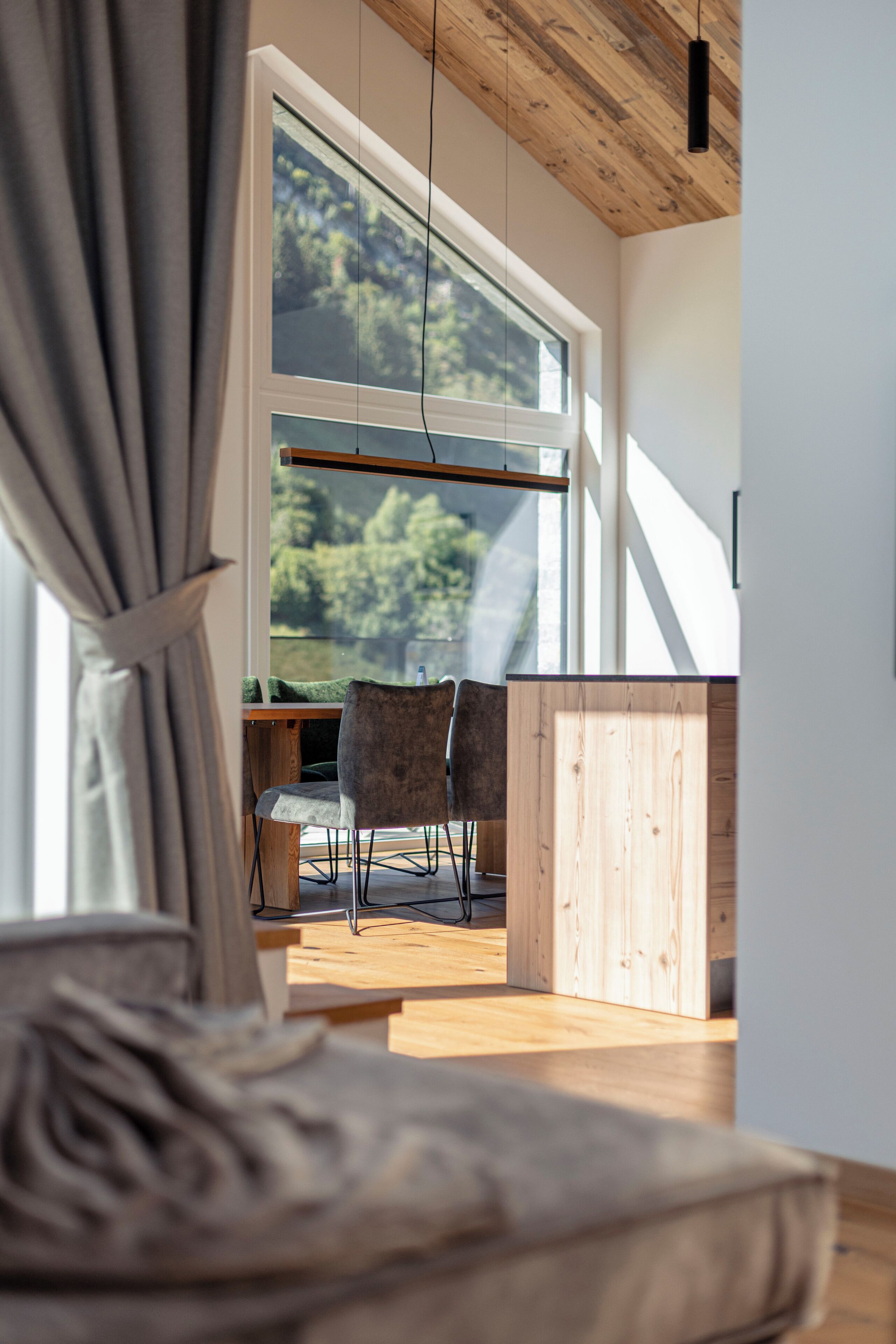 Een moderne kamer met een groot raam, houten plafond en een eethoek met stoelen en een tafel.
