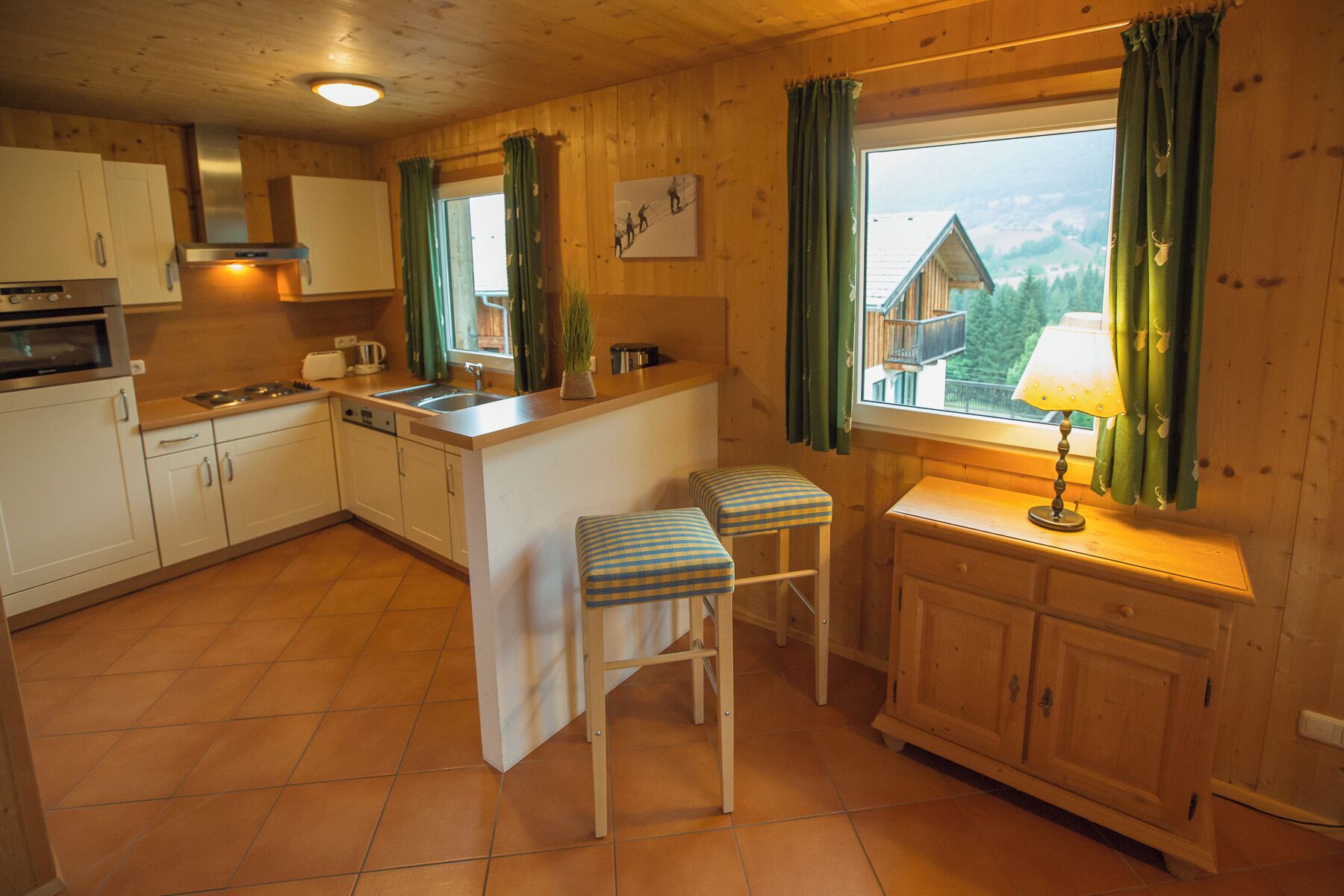 Une cuisine chaleureuse avec des meubles en bois, un îlot central et une fenêtre agrémentée de rideaux.