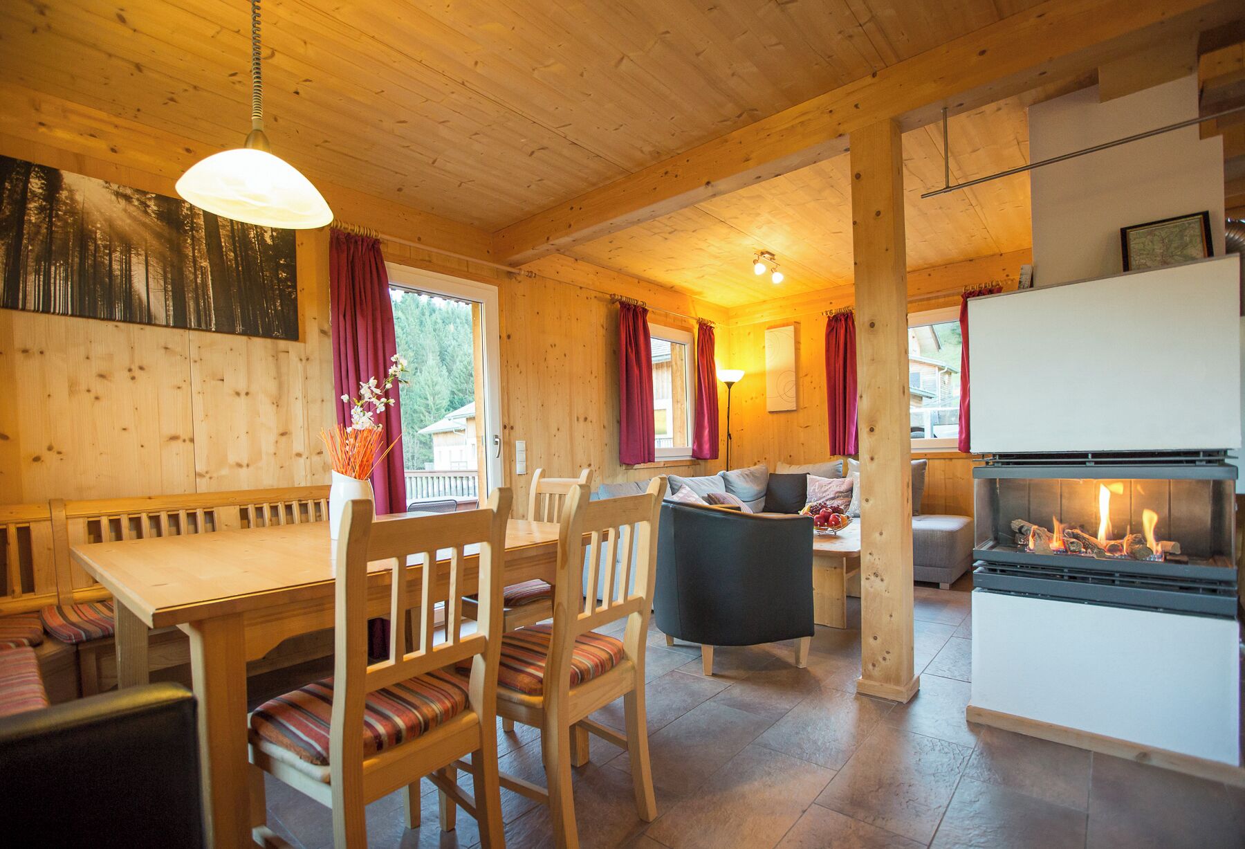 A cozy cabin interior with a wooden dining table, chairs, a sofa, and a fireplace.