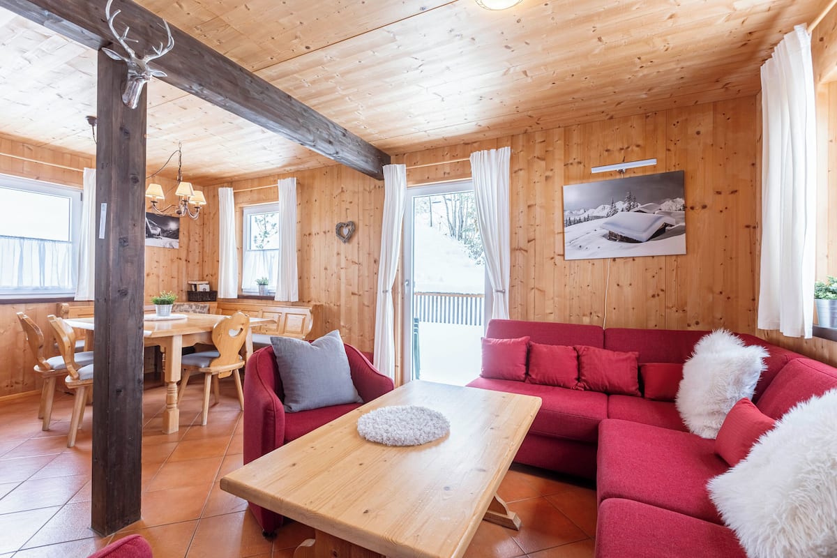 Un interior de madera con comedor, sofá rojo y una mesa con cojín blanco.