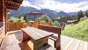 Una terraza de madera con mesa y bancos, con vistas a un paisaje montañoso.