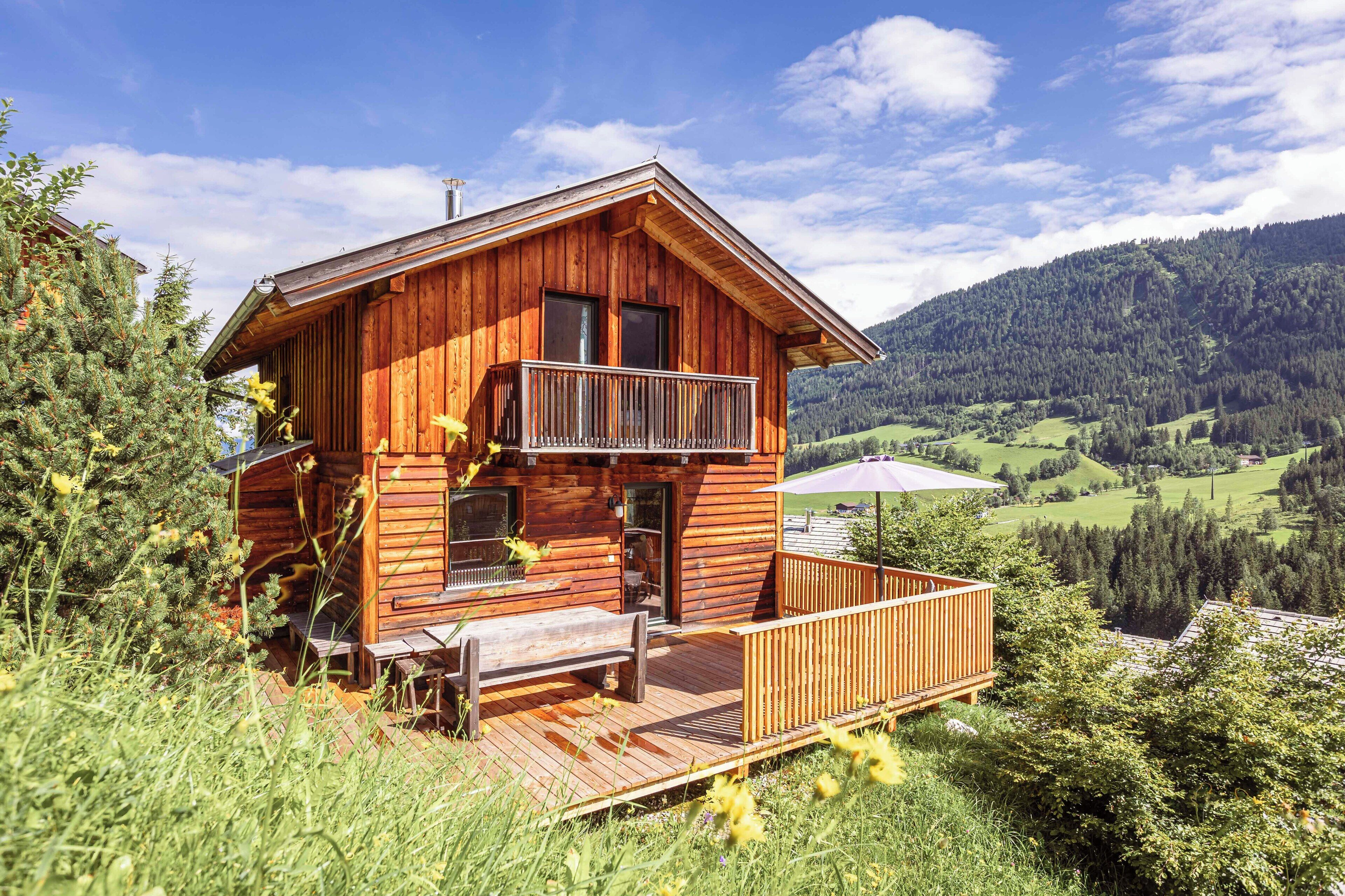 Een houten hut met een balkon, omgeven door weelderige begroeiing en een bergachtig landschap.
