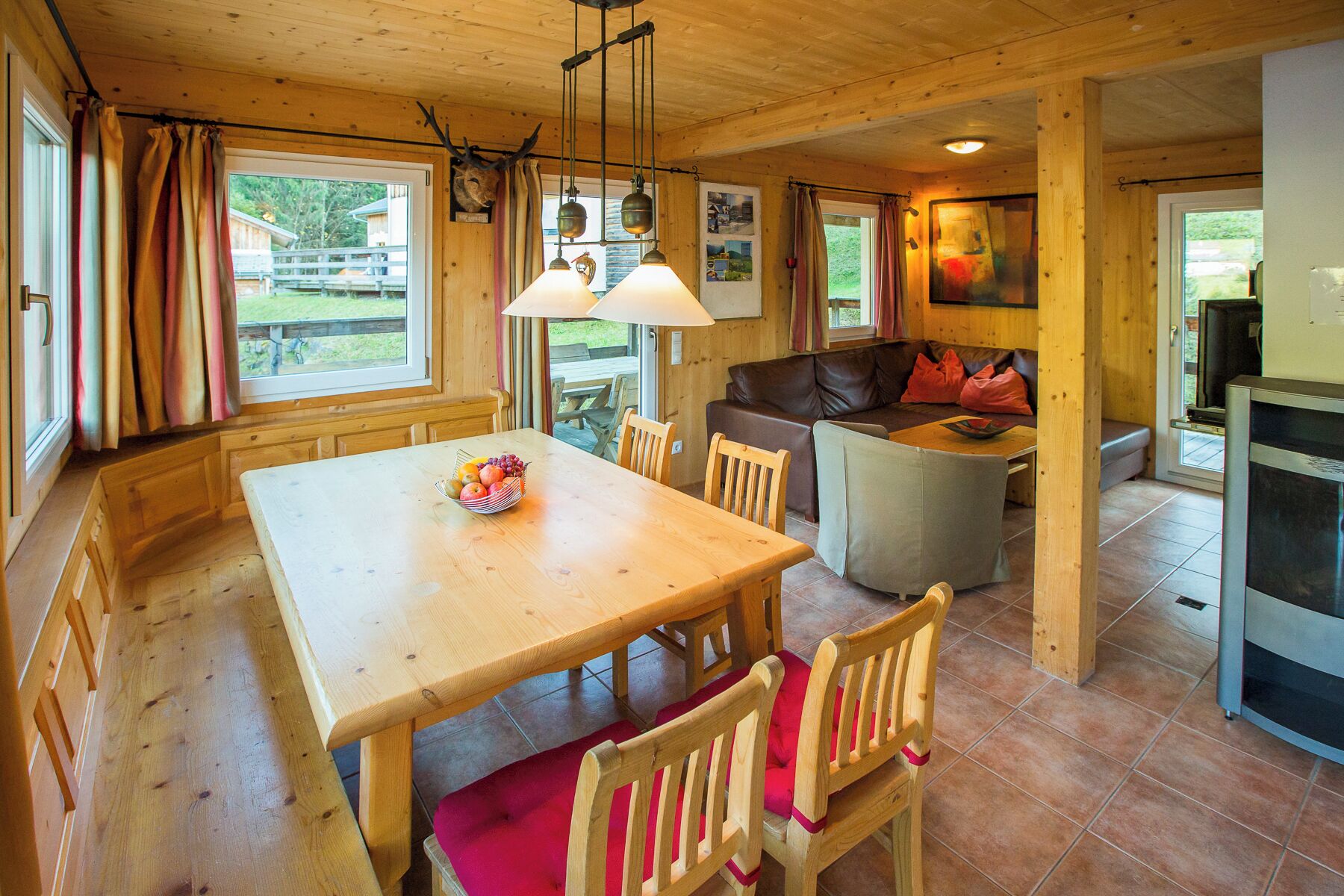 A wooden interior with a dining table, chairs, a sofa, and a television.