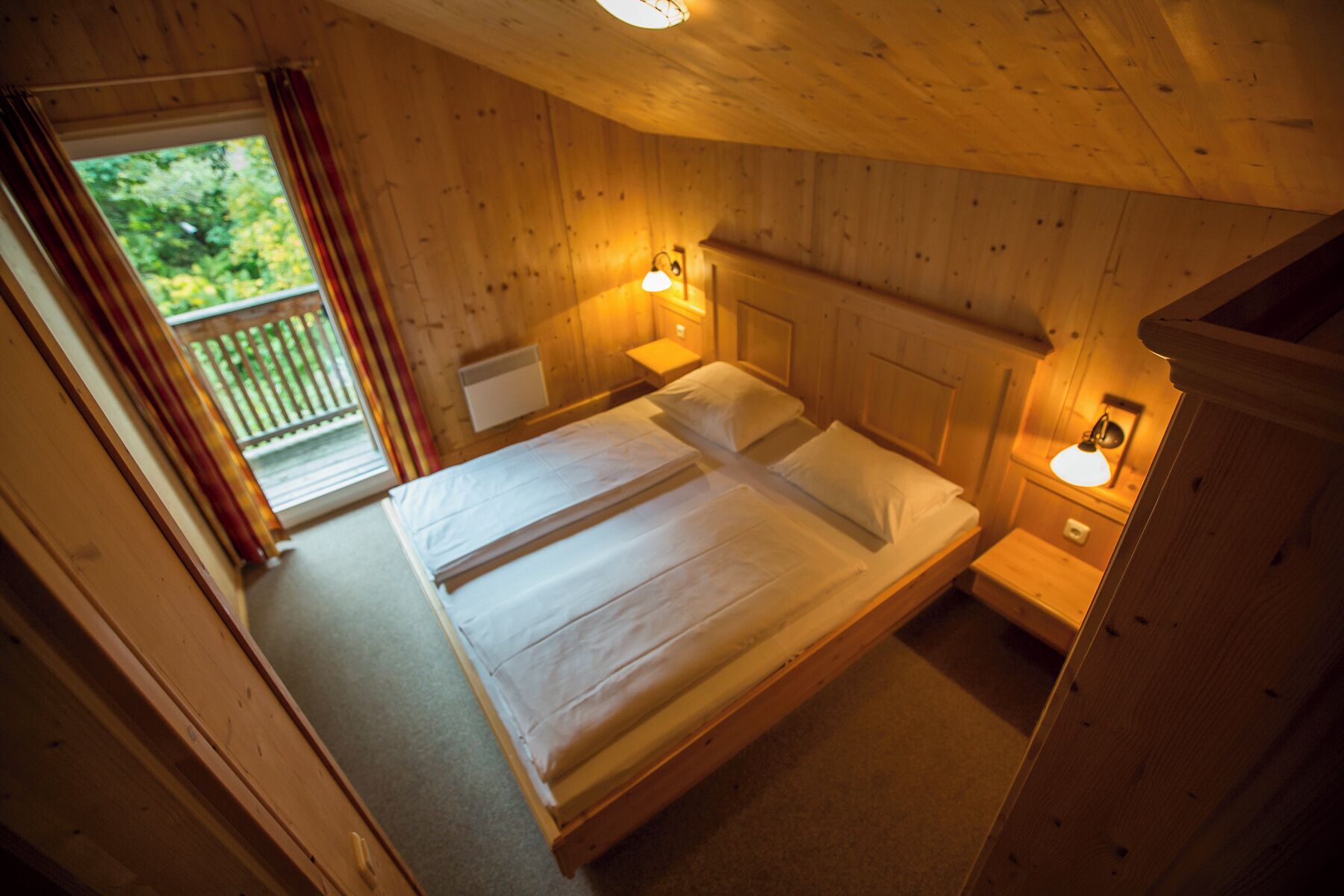 Ein Schlafzimmer einer Holzhütte mit einem Doppelbett, zwei Nachttischlampen und einem Fenster mit Vorhängen.