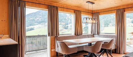 Un intérieur en bois comprenant une table à manger, des chaises et de grandes fenêtres donnant sur un paysage montagneux.
