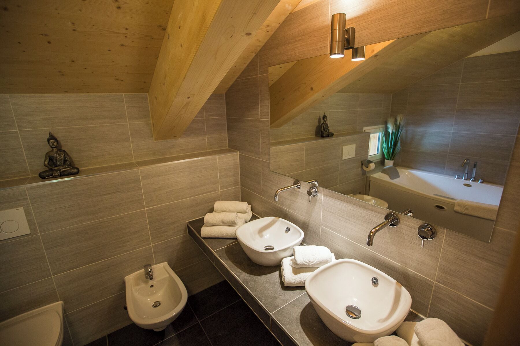 Une salle de bain moderne avec des poutres en bois, deux vasques, un bidet et un grand miroir.