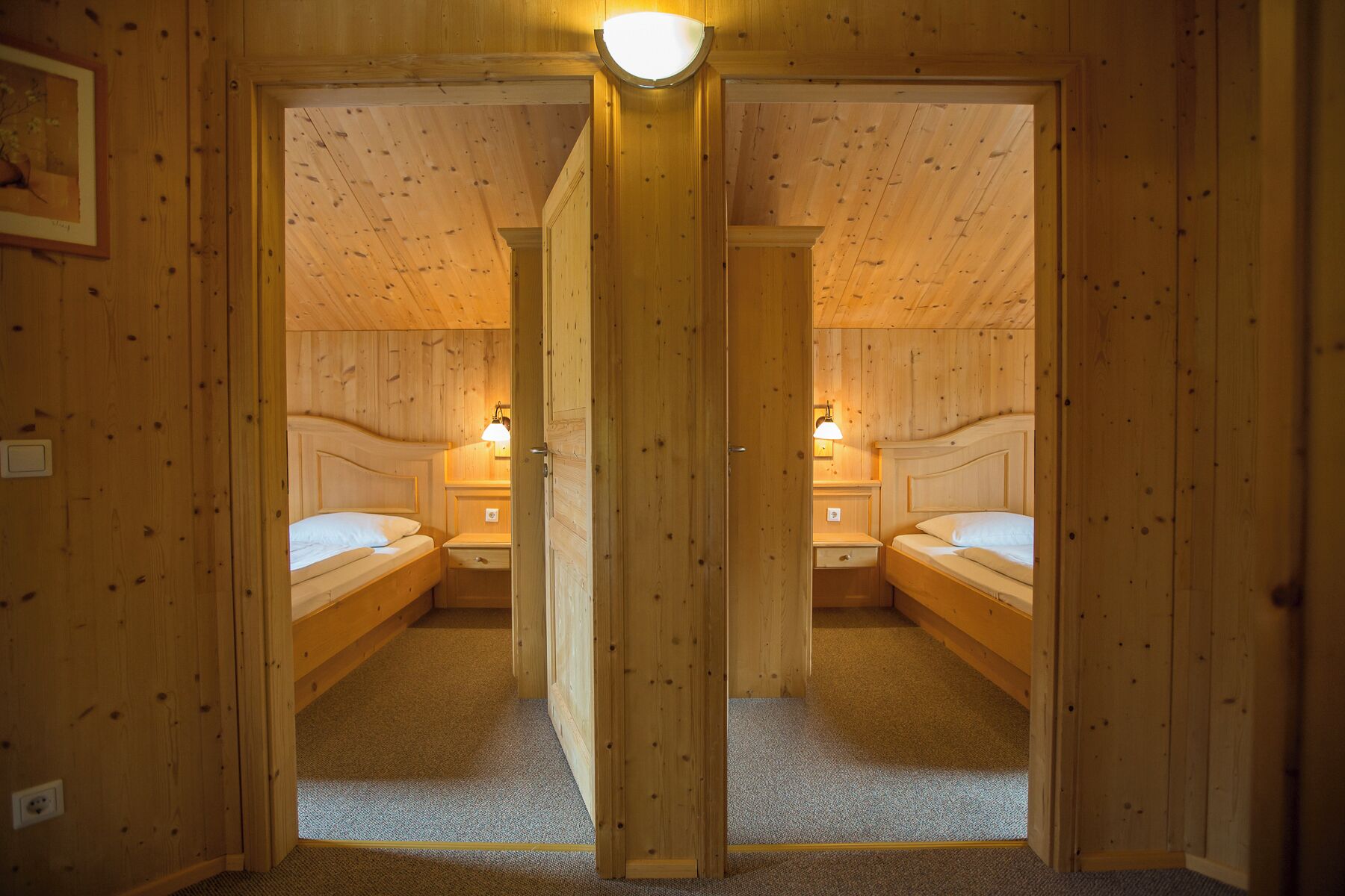 Habitación con espejos, dos camas, mesitas de noche y lámparas para cada una, y una puerta en el centro.