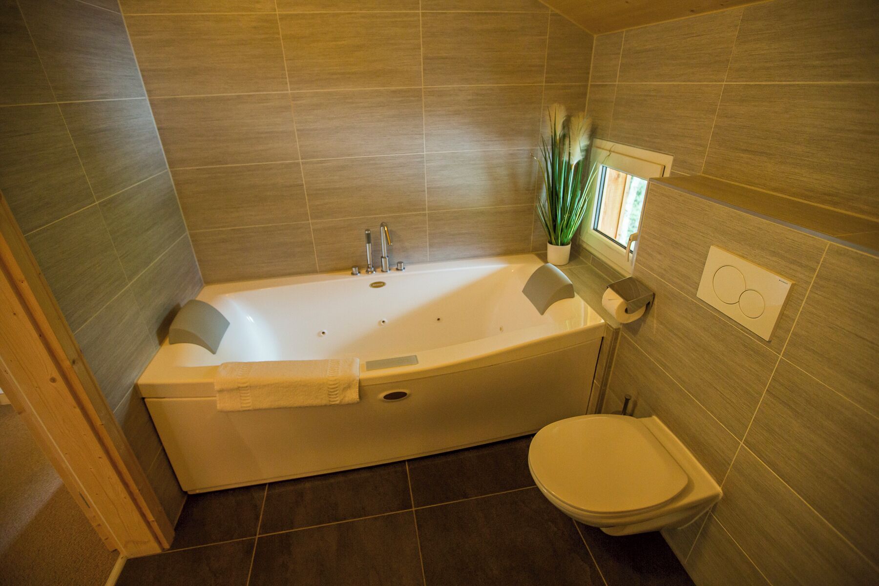 A bathroom with a bathtub, toilet, and a small window with a plant.